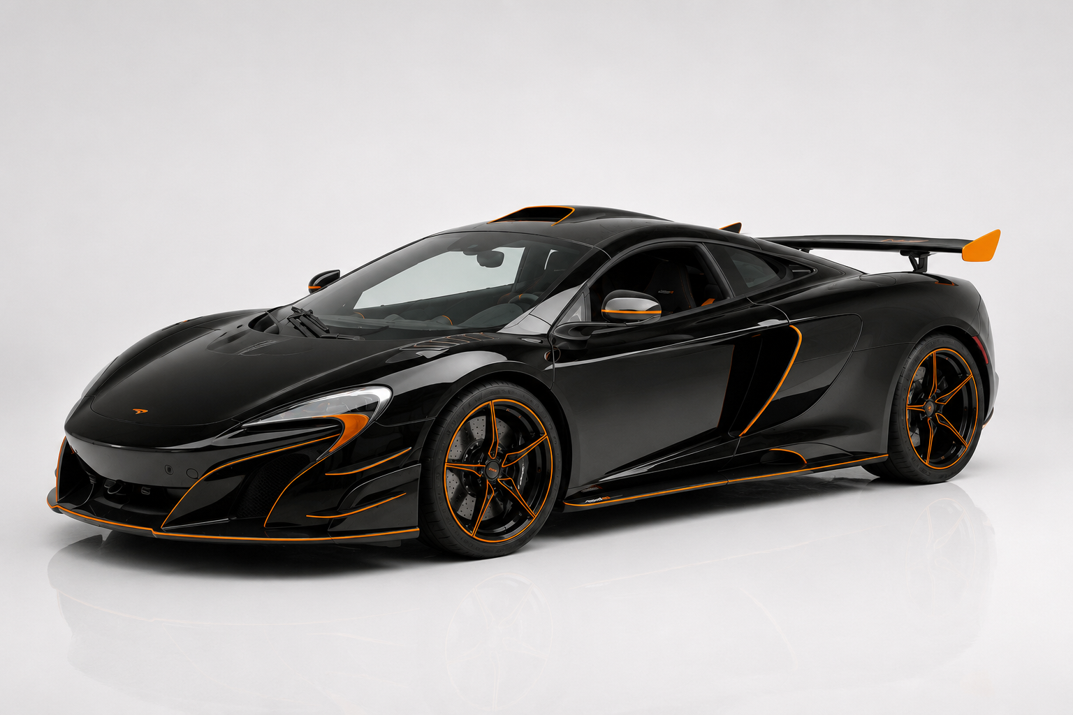 Gloss black McLaren 688 MSO HS with signature orange pinstripe accents along the front splitter, canards, side blades and five-spoke wheels, photographed in a studio in front three-quarter view showing the extended MSO carbon-fibre bodywork and fixed rear wing.