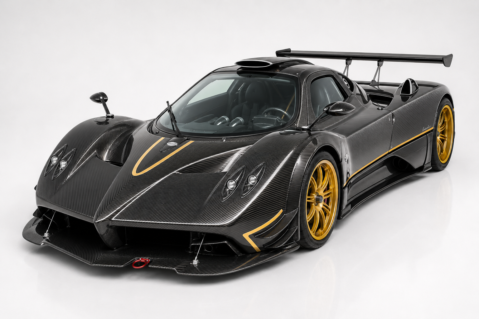 Exposed bare-carbon Pagani Zonda R with gold accent details and gold multi-spoke wheels in a studio setting, front three-quarter view showing the exaggerated front splitter, low ride height and tall track-only rear wing.