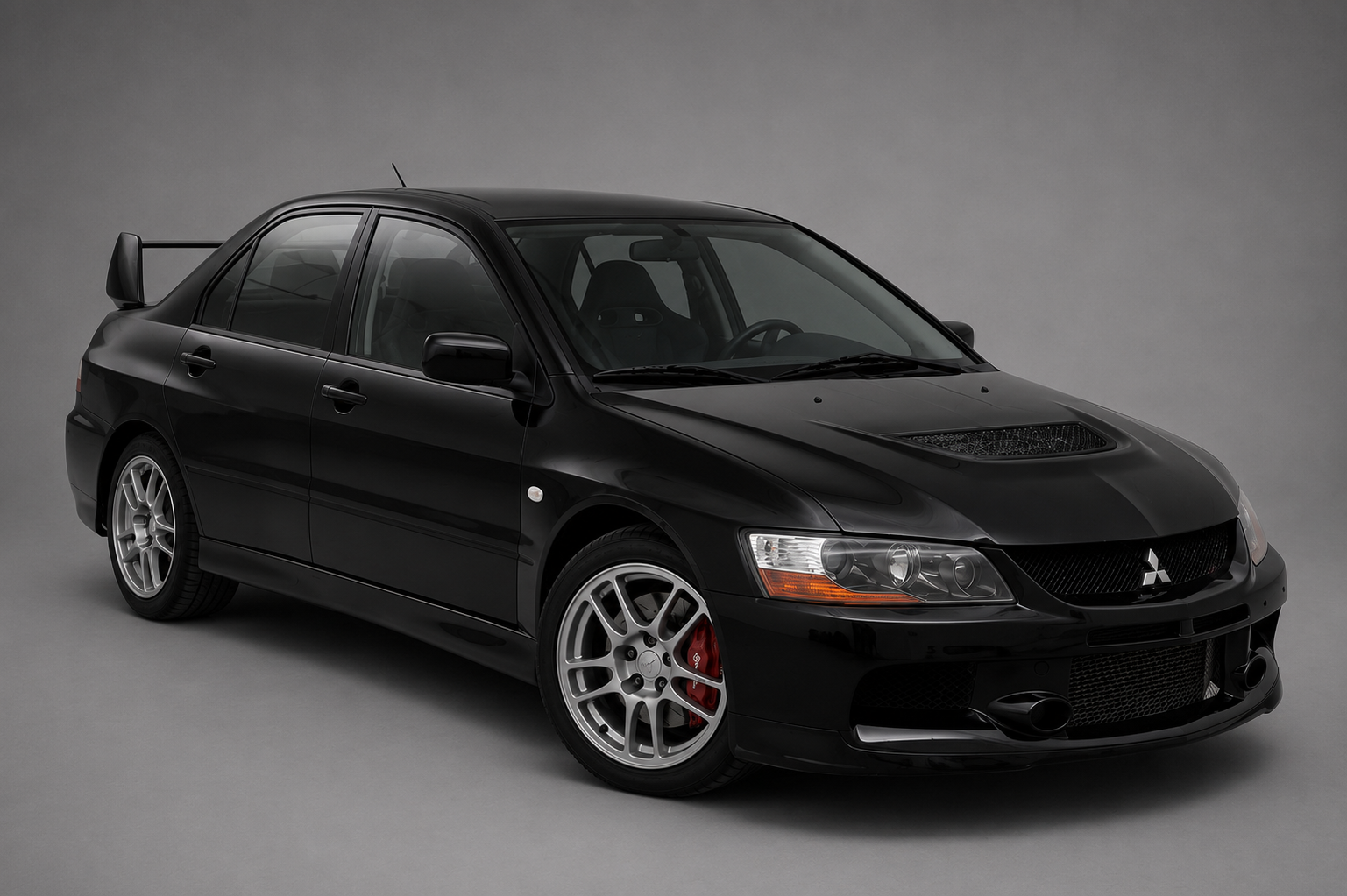 Studio three-quarter front view of a black Mitsubishi Lancer Evolution IX sedan with bonnet vent, silver alloy wheels, red brake calipers and rear wing above the roofline on a plain grey backdrop.