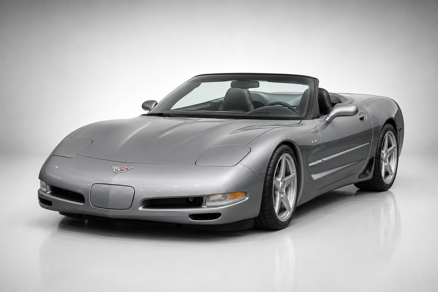Silver Chevrolet Corvette C5 convertible in a studio setting, front three-quarter view, showing pop-up headlights, chrome badging and silver five-spoke alloy wheels, with the roof stowed.