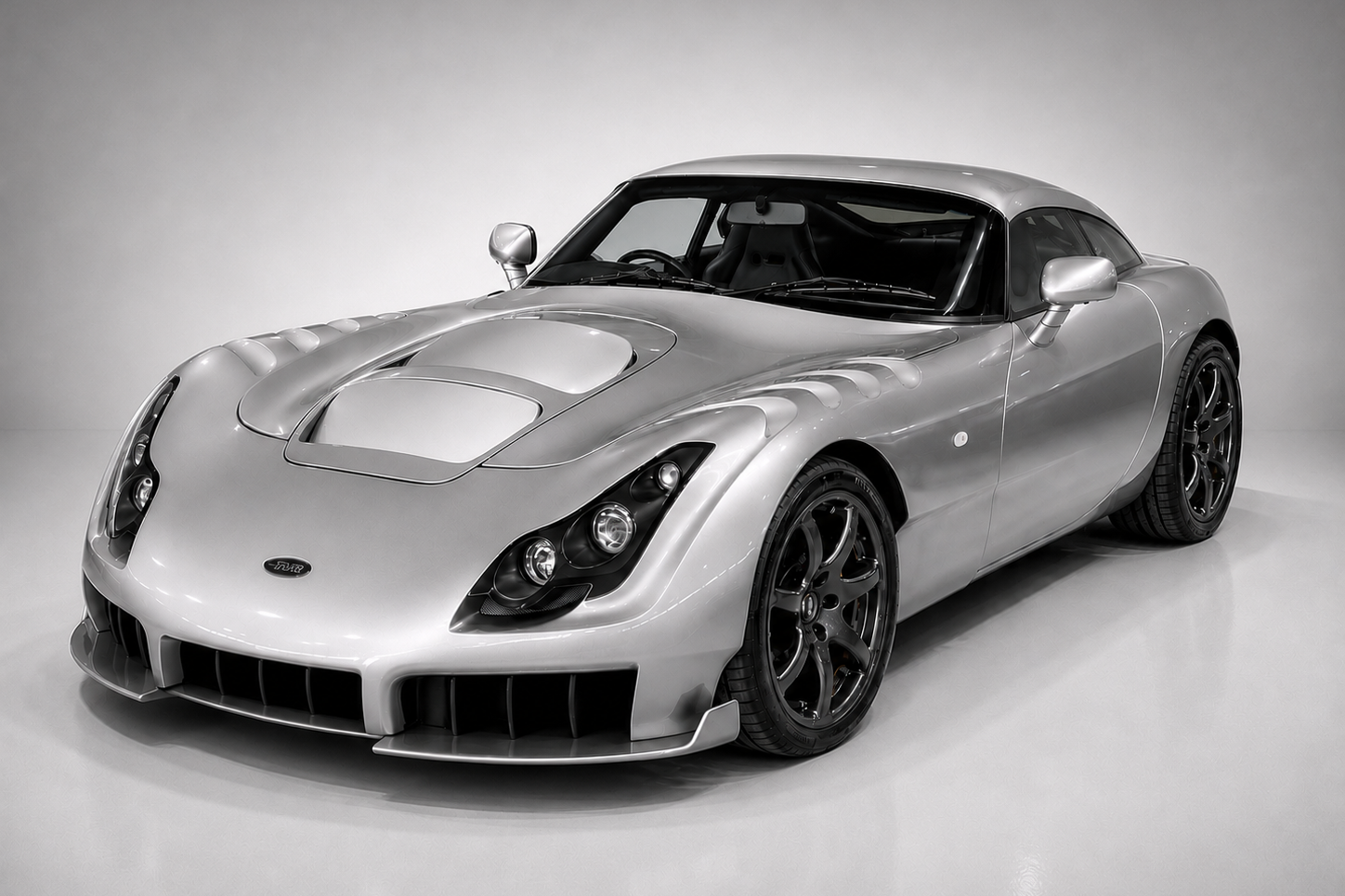 Silver TVR Sagaris in a studio setting, front three-quarter view showing the sculpted composite bodywork, bonnet ducts, wing-mounted gills, aggressive front splitter and black alloy wheels.