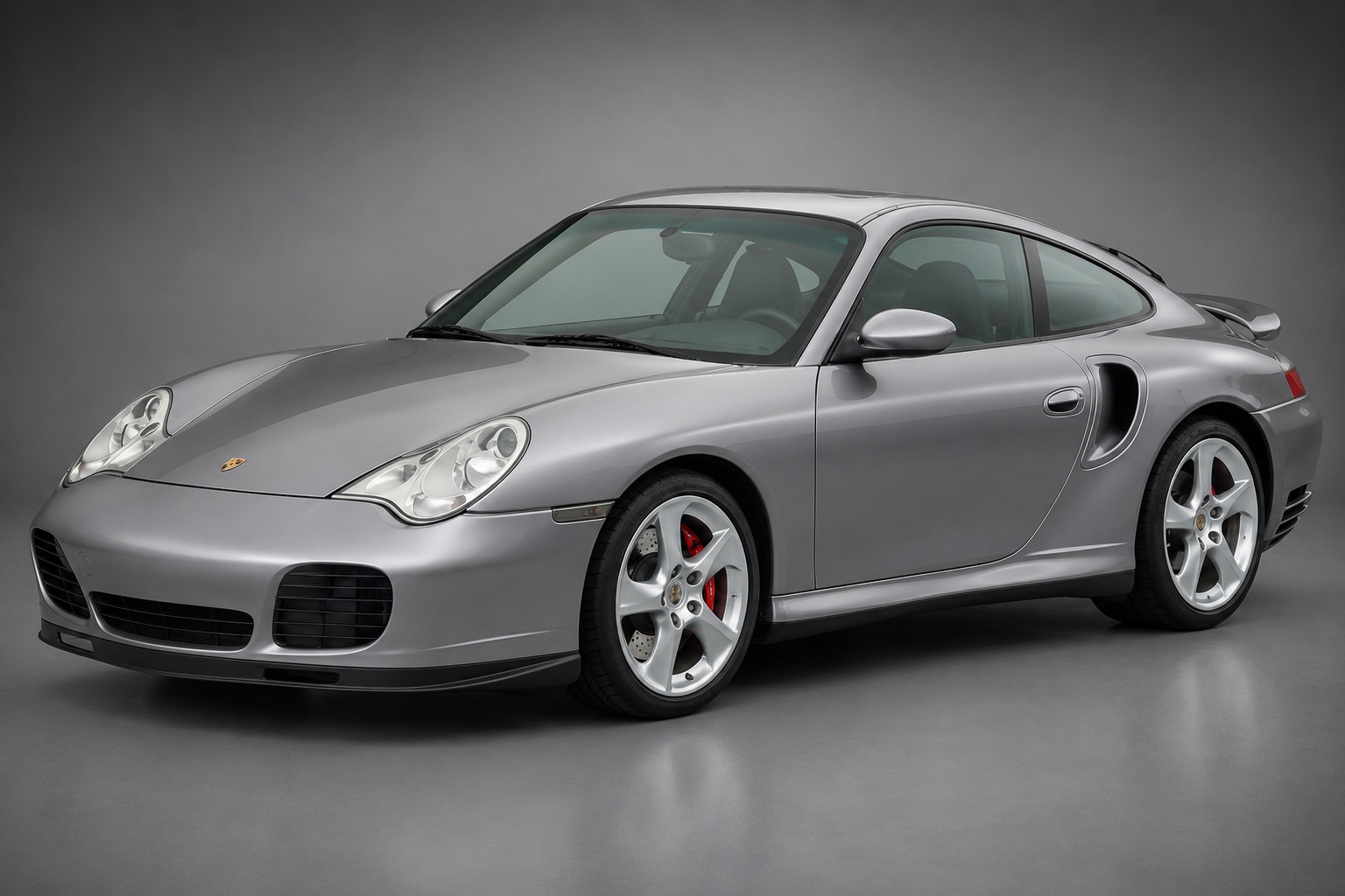 Silver Porsche 911 (996) Turbo coupe in a grey studio setting, front three-quarter view showing the fixed headlights, red brake calipers and five-spoke alloy wheels.