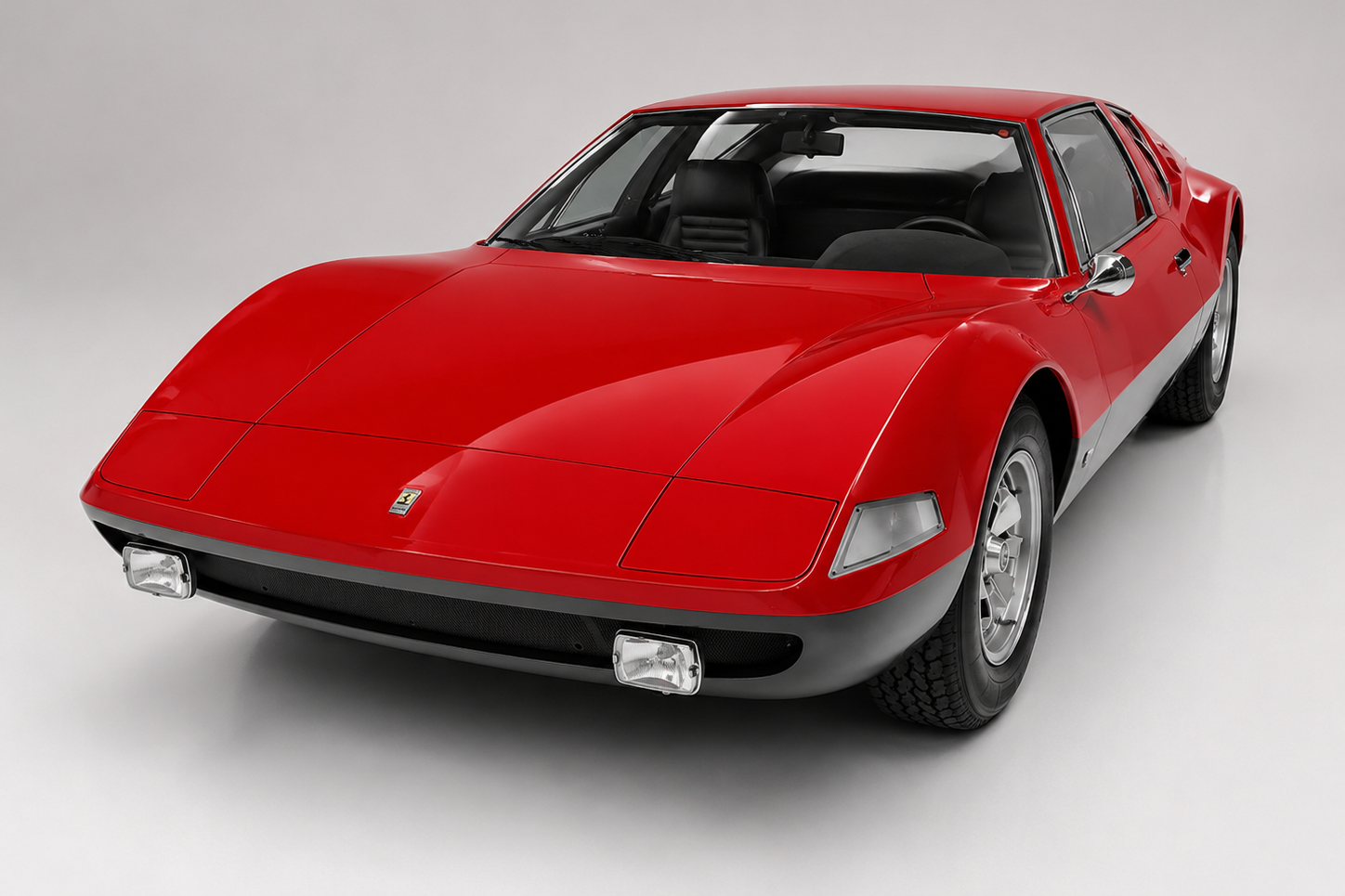 Red Monteverdi Hai 450 SS photographed in a studio, front three-quarter view showing the low wedge nose, twin square headlamps behind clear covers, small yellow Ferrari-style badge on the nose panel, side louvres and five-spoke alloy wheels.