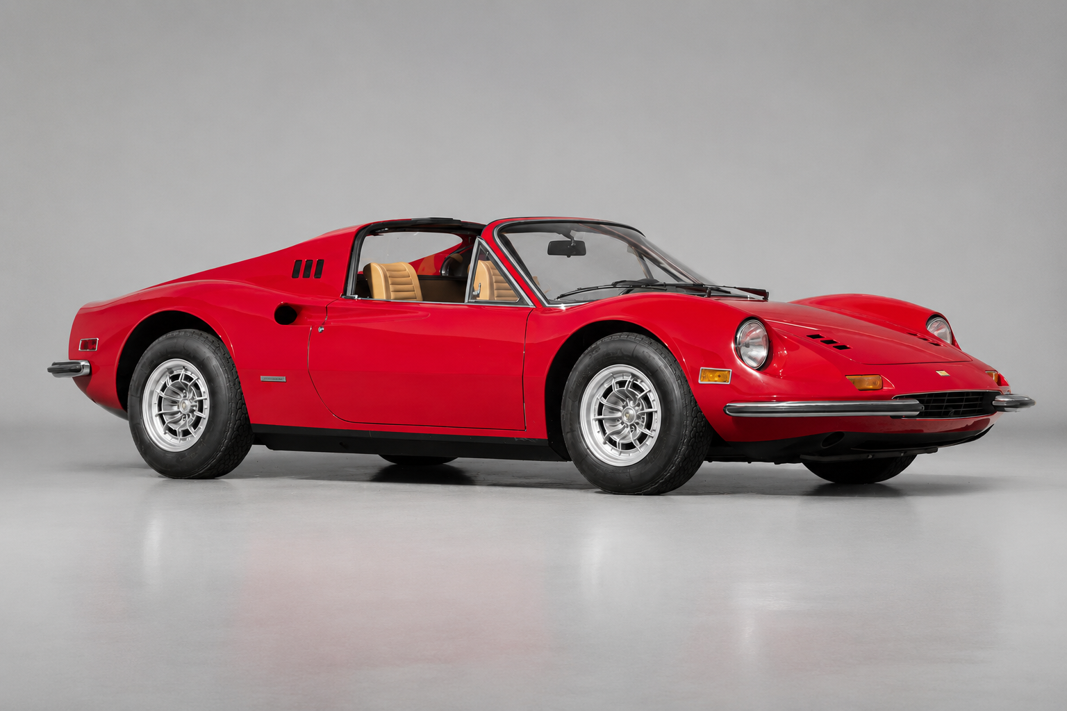 Red Dino 246 GTS, front three-quarter studio view on a grey backdrop with the targa roof panel removed, showing the Pininfarina bodywork, sail-panel louvres, chrome bumpers, Cromodora alloy wheels and tan interior.