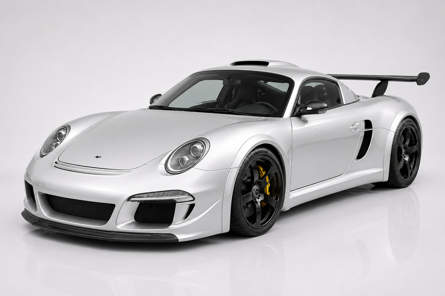 Silver RUF CTR3 Clubsport in a studio setting, front three-quarter view showing the mid-engine supercar silhouette with 997-derived front end, aggressive front splitter and side vents, wide rear arches, tall carbon rear wing and dark five-spoke wheels — RUF's first bespoke ground-up supercar.