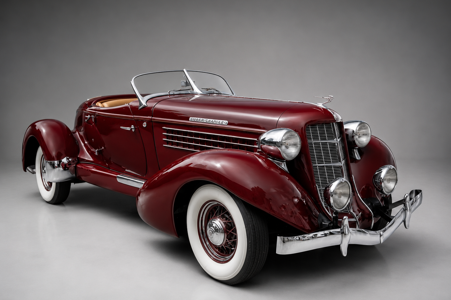 Deep burgundy Auburn 851 Speedster in a studio setting, front three-quarter view showing the sweeping fenders, chrome supercharger exhaust pipes badge, twin headlamps and whitewall wire wheels.