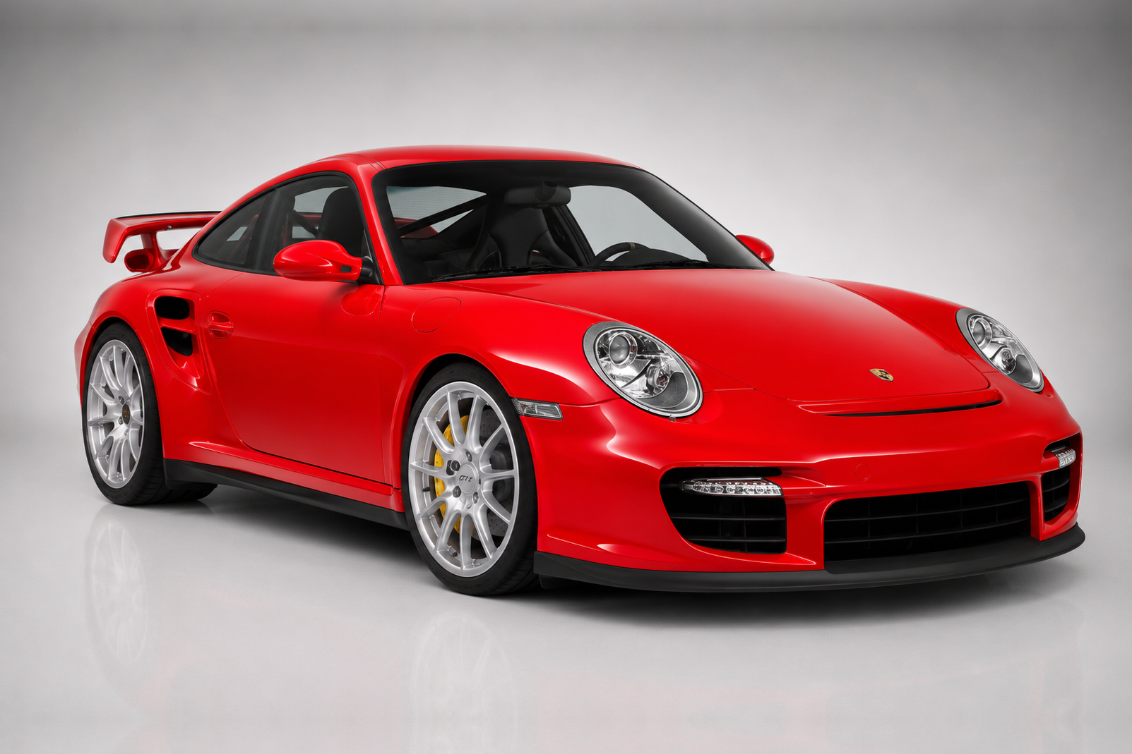Red Porsche 911 GT2 (997) in a studio, front three-quarter view showing the deep front splitter with LED daylight running lights, side intercooler intakes, fixed rear wing and forged silver wheels.