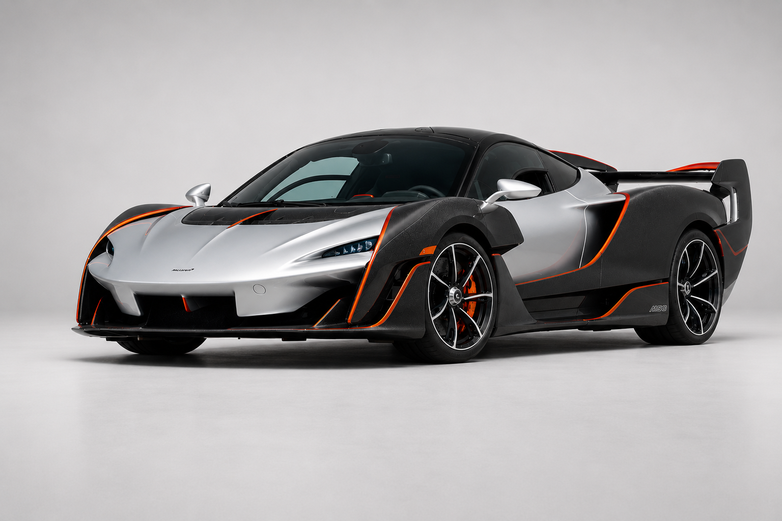McLaren Sabre in a studio setting, front three-quarter view in silver over exposed carbon with orange accents, showing dihedral doors, side intakes and full-width rear wing.