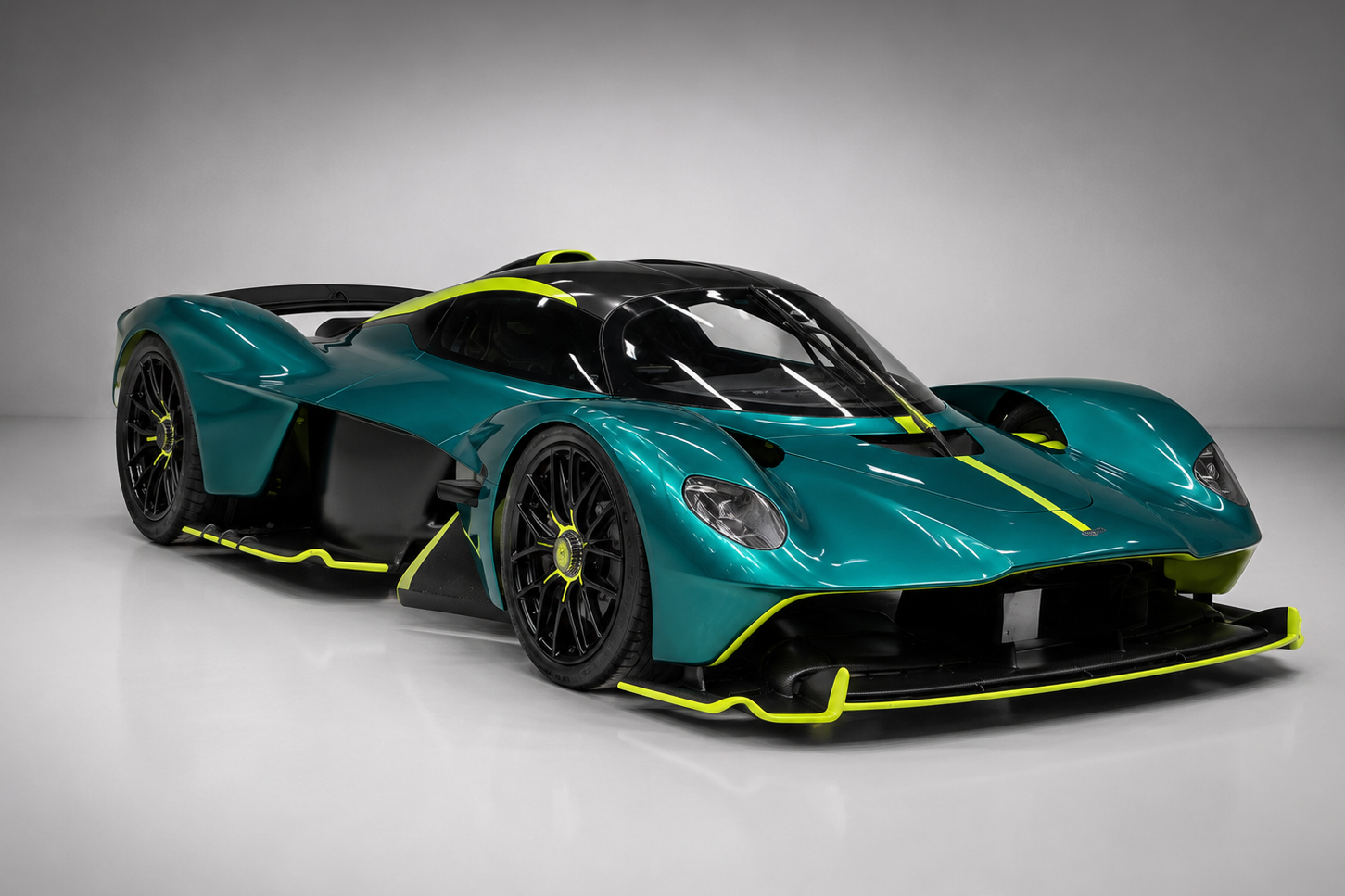 Teal Aston Martin Valkyrie in a studio setting, front three-quarter view showing the extreme aerodynamic bodywork, exposed carbon fibre, neon-green accents, black multi-spoke wheels and low-slung prototype-derived proportions.
