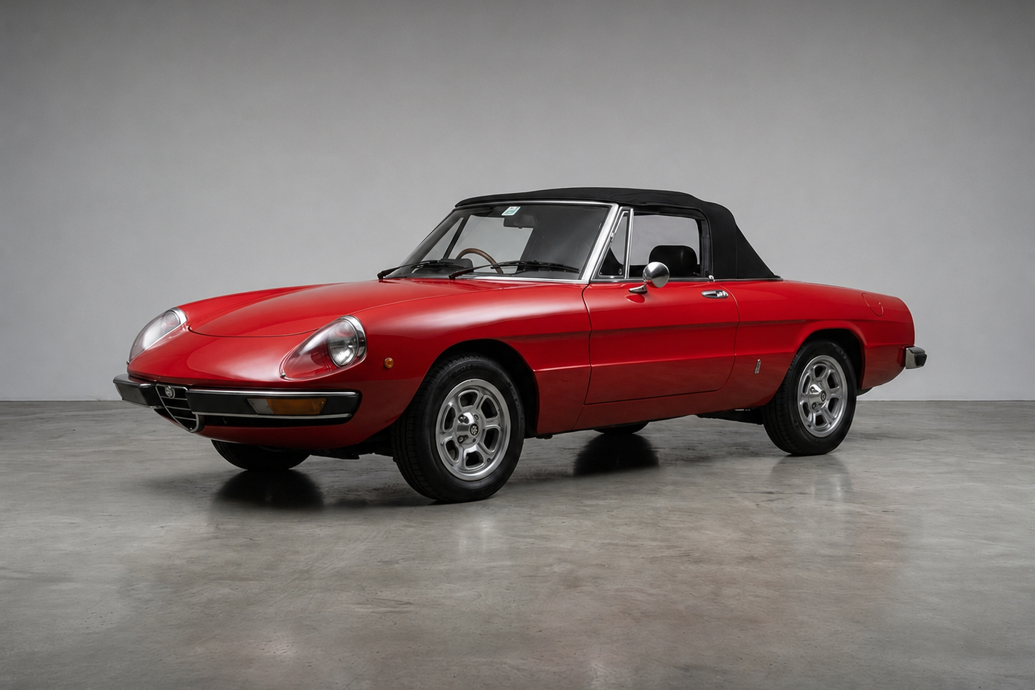 Red Alfa Romeo Spider (105/115 Series) with black hood raised, front three-quarter studio view, showing the smooth low nose, alloy wheels and chrome trim.