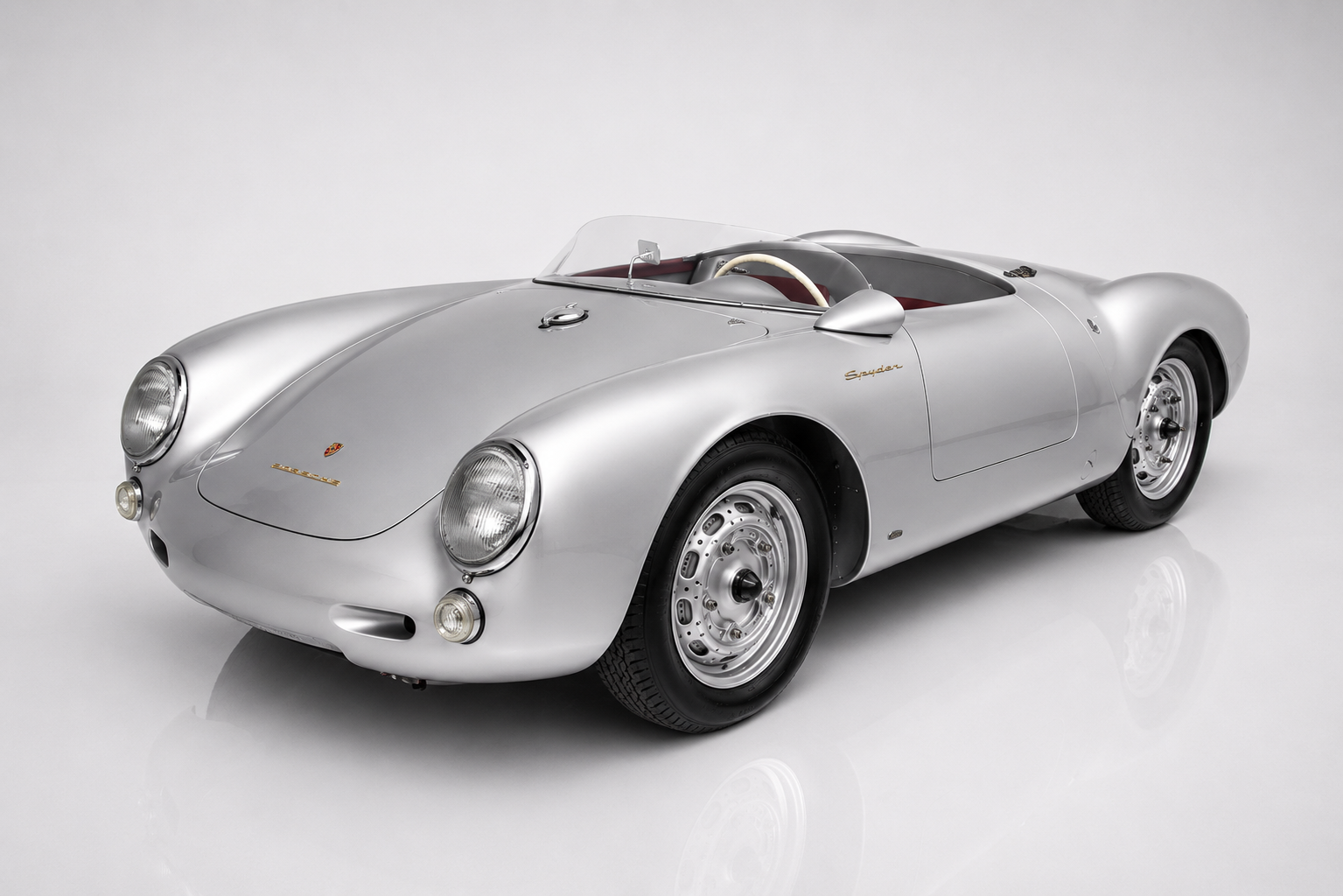 Silver Porsche 550 Spyder in a studio setting, front three-quarter view showing the low aluminium bodywork, twin headlamps, aeroscreen and centre-lock steel wheels.