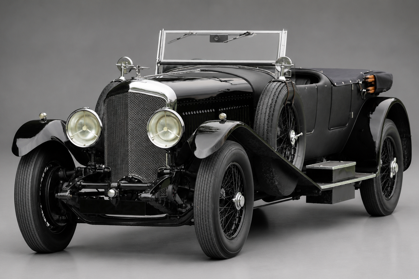 Black Bentley 8 Litre open tourer, front three-quarter studio view showing the tall chrome radiator with mesh grille, twin headlamps, side-mounted spare wheel, running board and black wire wheels.