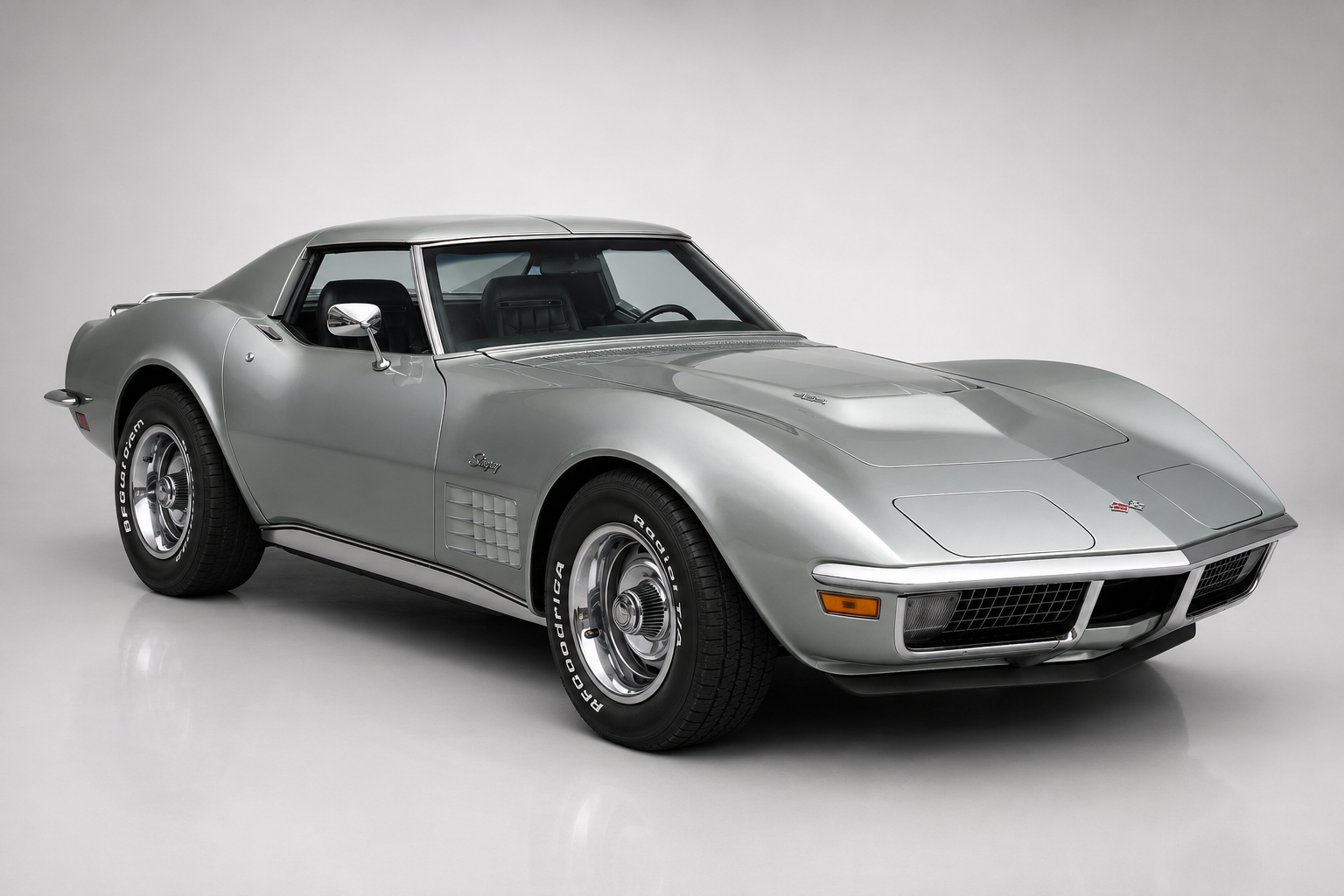 Silver Chevrolet Corvette Stingray C3 T-top coupe, front three-quarter studio view showing the shark-styled bodywork, chrome side mirror, side fender louvres, chrome bumper and polished five-spoke wheels on a plain grey backdrop.