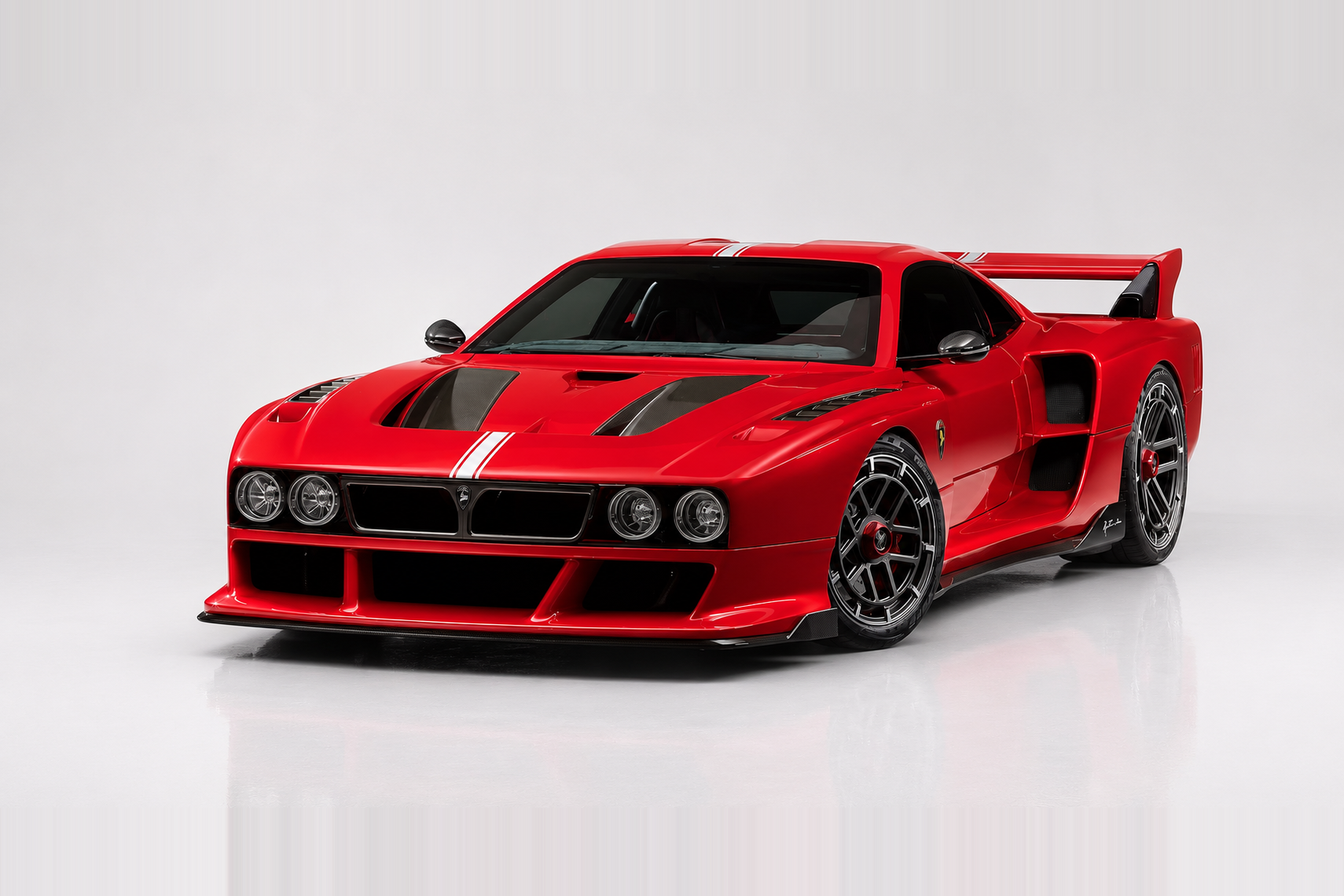 Red Kimera K39 in a bright studio, front three-quarter view showing a wide low-slung supercar body with dual white stripes on the bonnet, quad round headlights either side of a black grille, deep front splitter, aggressive side intakes, flared arches over multi-spoke black wheels with red brake calipers and a shark-fin cabin profile.