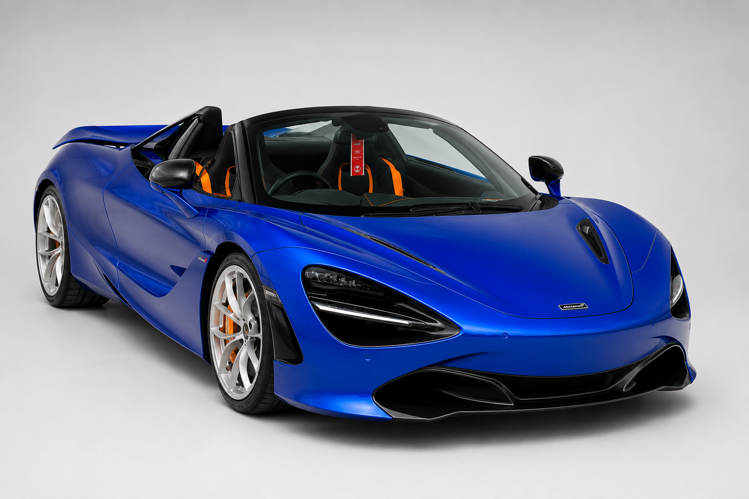 Blue McLaren 720S Spider in a studio setting, roof down, front three-quarter view showing its orange-trimmed cabin and silver alloy wheels.