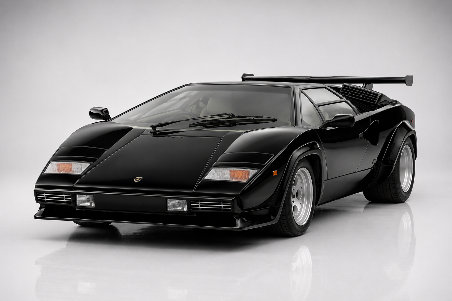 Black Lamborghini Countach LP5000 QV in a bright studio, front three-quarter view showing the wedge silhouette, pop-up headlamps, wide flared arches, chin spoiler, oversized rear wing on tall uprights and telephone-dial silver alloy wheels.