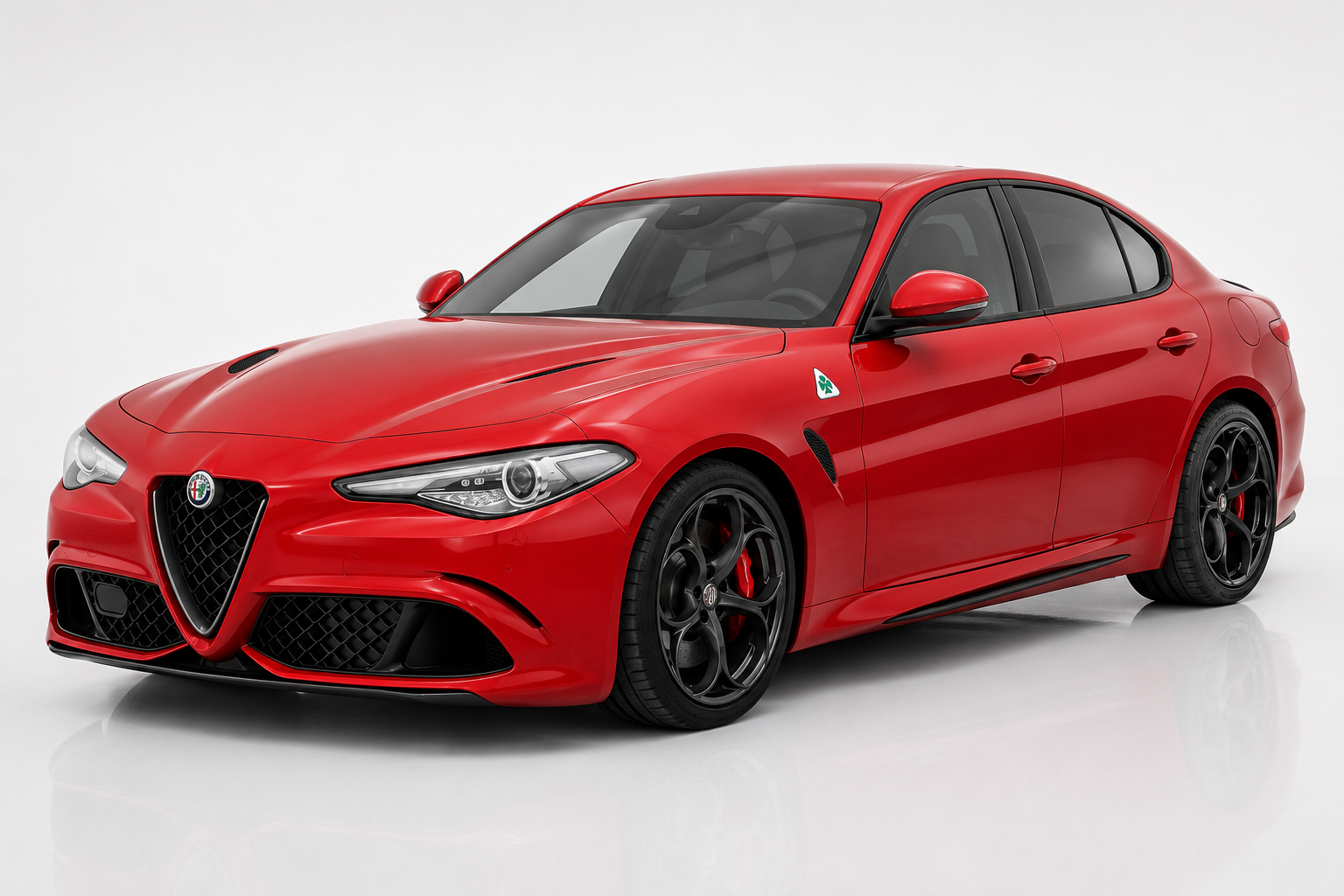 Red Alfa Romeo Giulia Quadrifoglio saloon in a bright studio, front three-quarter view showing the shield grille, LED headlights, carbon front splitter, side gill vent behind the front wheel and dark five-hole alloy wheels with red brake calipers.