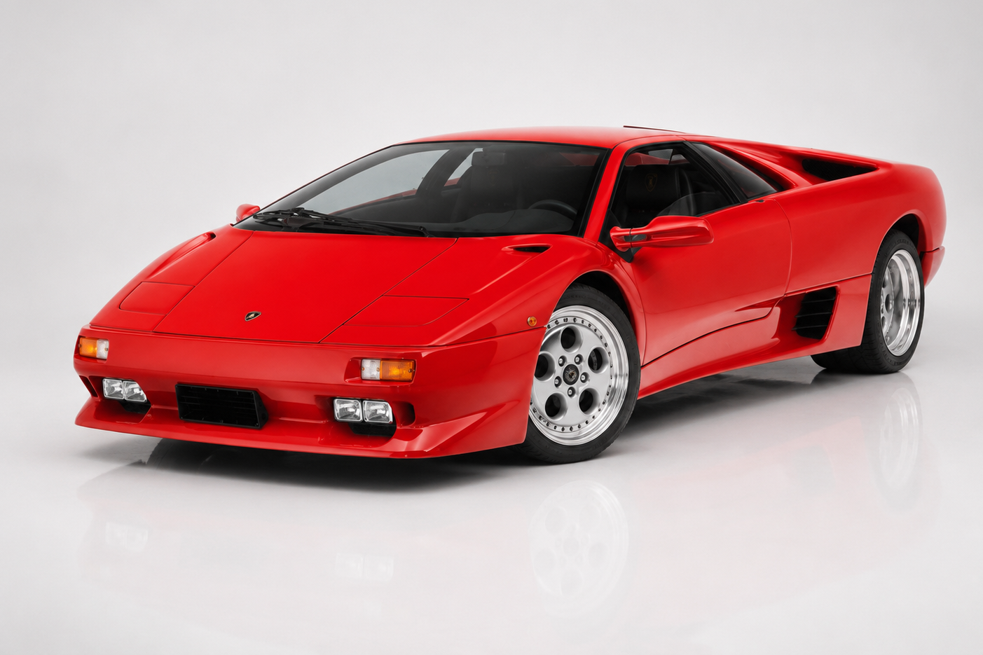 Red Lamborghini Diablo photographed in a studio, front three-quarter view showing the low wedge nose, pop-up headlamps era front lamps, scissor-door coupe silhouette and five-hole split-rim alloy wheels.