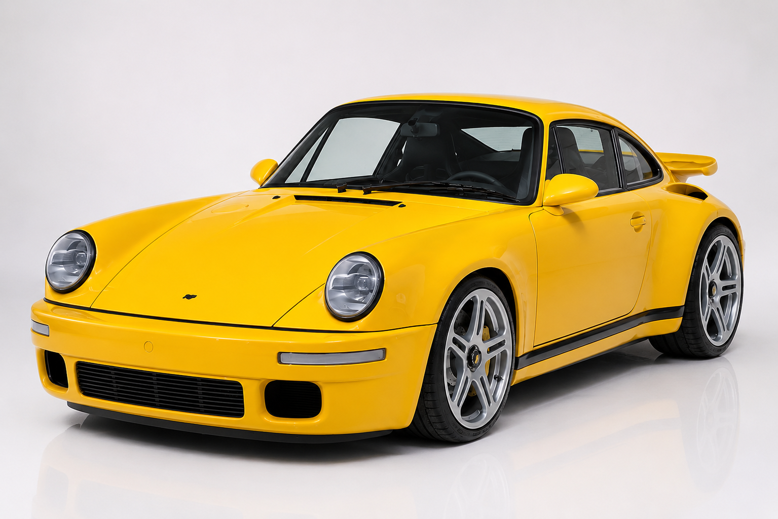 Yellow RUF CTR 'Yellowbird' in a studio setting, front three-quarter view showing the narrow-body 911 Carrera 3.2 silhouette with flush-fit bumpers, integrated fog and driving lights, RUF five-spoke wheels and a subtle ducktail spoiler — the 1987 Road & Track Ehra-Lessien world's-fastest test winner.