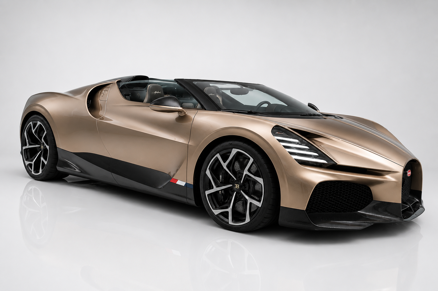 Bronze-gold Bugatti W16 Mistral open roadster, front three-quarter studio view showing the sweeping roofless silhouette, twin engine intake scoops behind the cabin, horseshoe grille, French tricolour side flash, black lower carbon bodywork and multi-spoke alloy wheels on a light reflective backdrop.