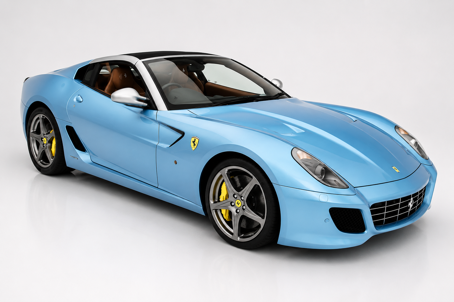 Azzurro-blue Ferrari 599 SA Aperta open-top photographed in a studio, front three-quarter view showing the more steeply raked windscreen, aluminium bootlid area, unique five-spoke wheels and yellow brake calipers.