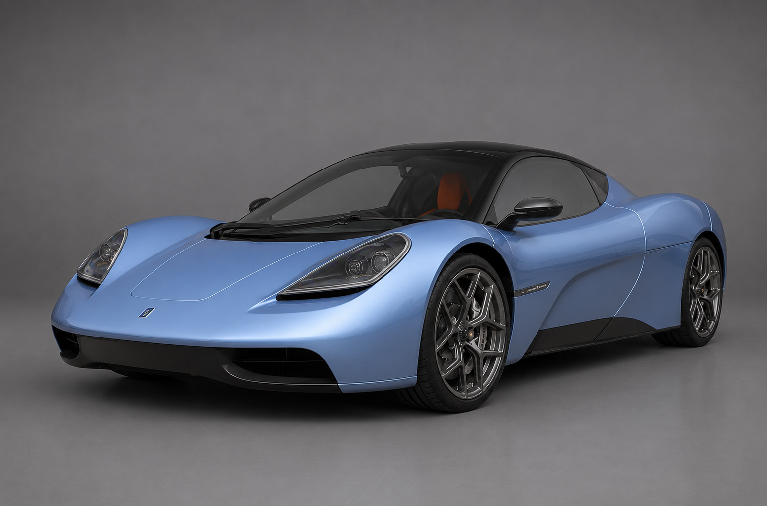 Powder-blue Gordon Murray Automotive T.50 supercar with a gloss-black roof, front three-quarter studio view showing the low nose, oval headlamps and multi-spoke alloy wheels against a plain grey backdrop.