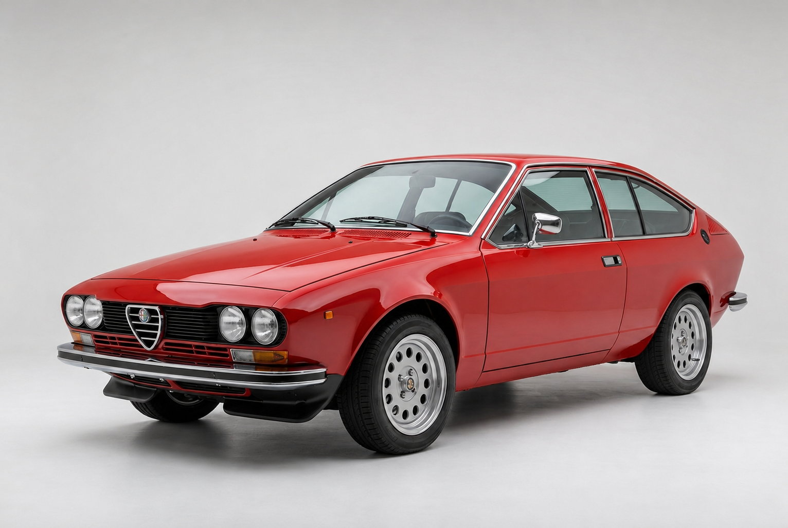 Red Alfa Romeo Alfetta GT fastback coupé in a studio, front three-quarter view showing the Giugiaro-designed body with four round headlamps, Alfa Romeo shield in the centre grille, chrome bumper and multi-spoke alloy wheels.