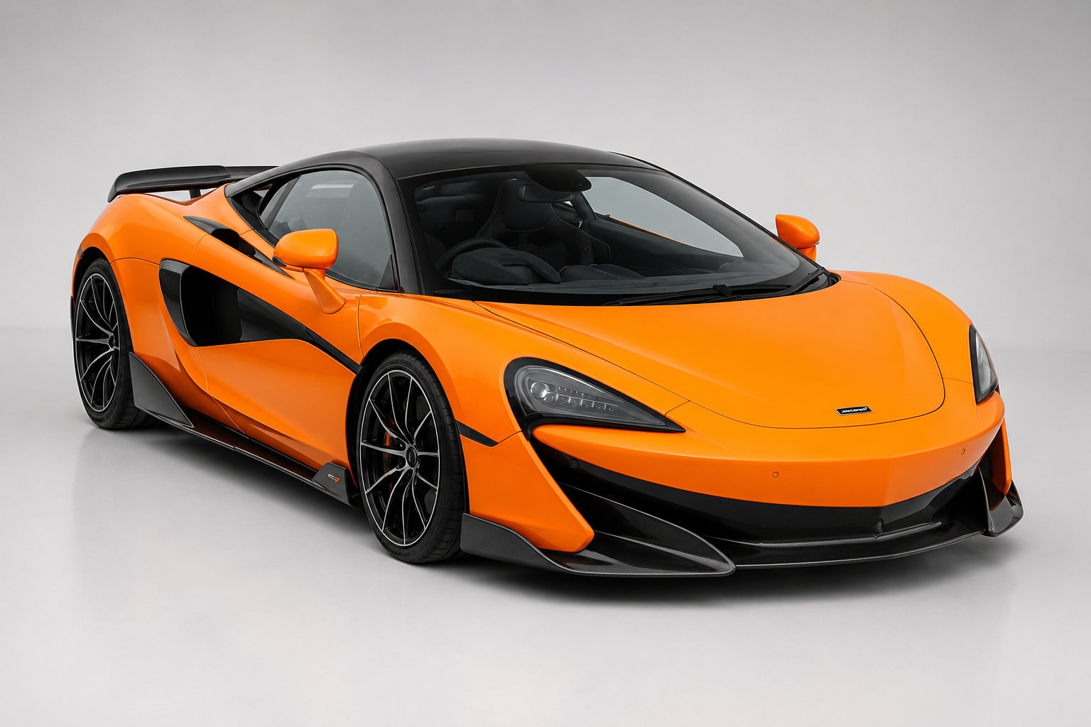 Orange McLaren 600LT with black roof in a studio setting, front three-quarter view with carbon aero, side intakes and dark alloy wheels.
