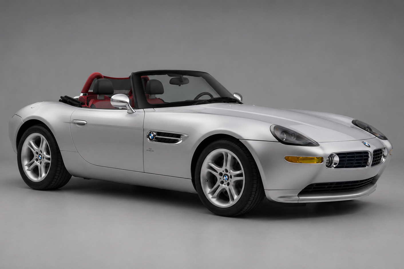 Silver BMW Z8 roadster with the top down and red leather interior, front three-quarter studio view on a plain grey backdrop.