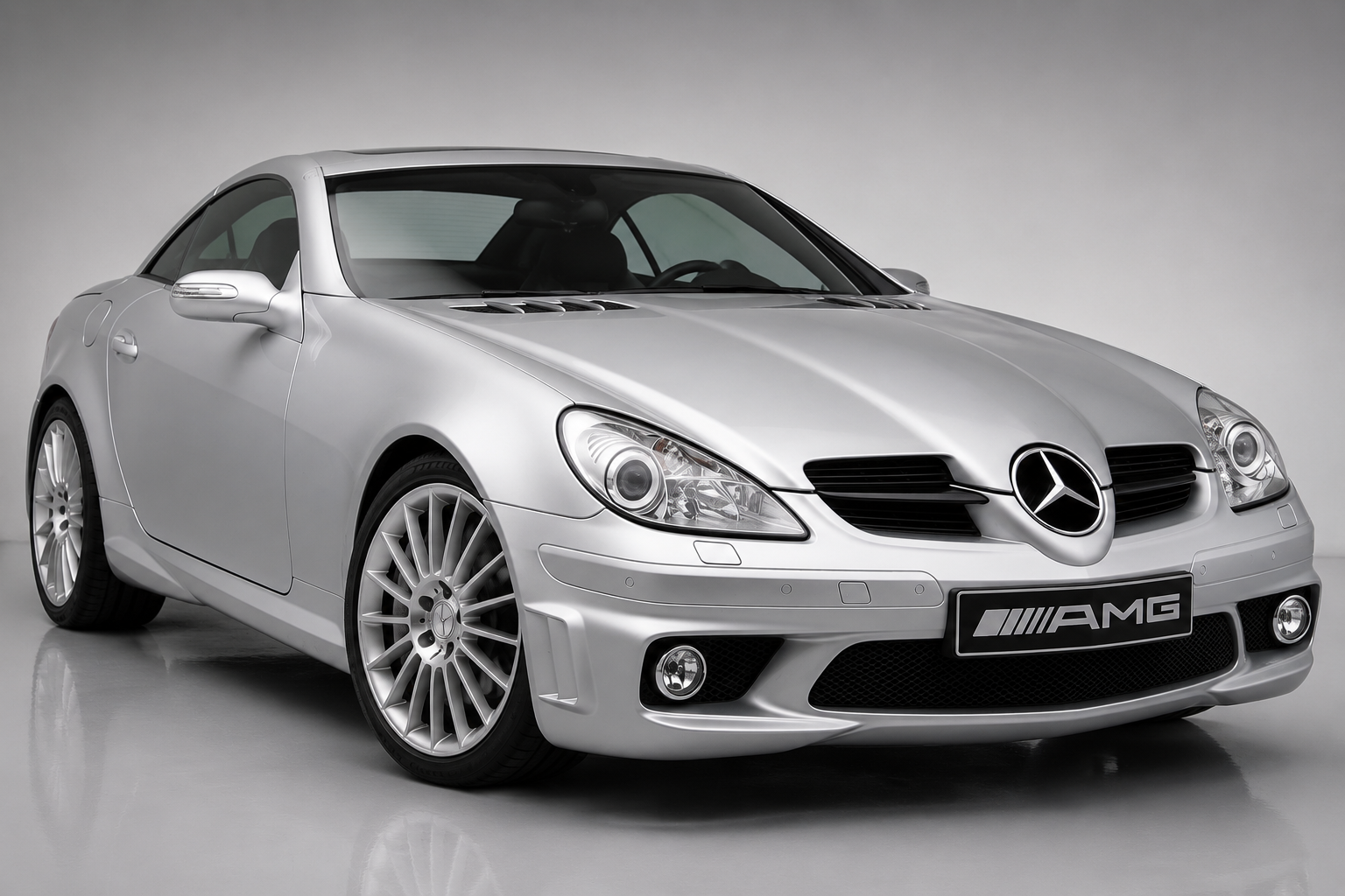 Silver Mercedes-Benz SLK 55 AMG (R171) studio shot, front three-quarter view showing AMG grille badge, multi-spoke alloy wheels and the folding hardtop raised.