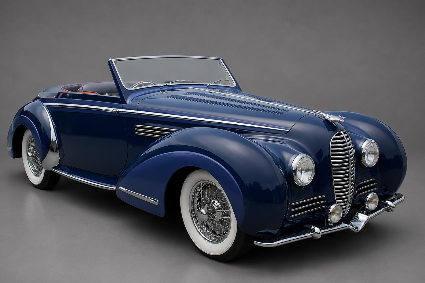 Dark blue Delahaye 135 cabriolet with top down, front three-quarter studio view on a plain grey backdrop showing chromed grille, wire wheels and whitewall tyres.