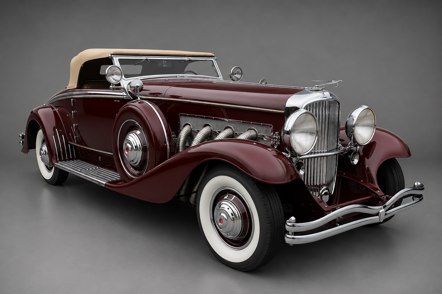 Maroon Duesenberg Model SJ convertible coupe with tan soft top raised, front three-quarter studio view on a plain grey backdrop showing external supercharger exhaust pipes, chromed grille and whitewall tyres.