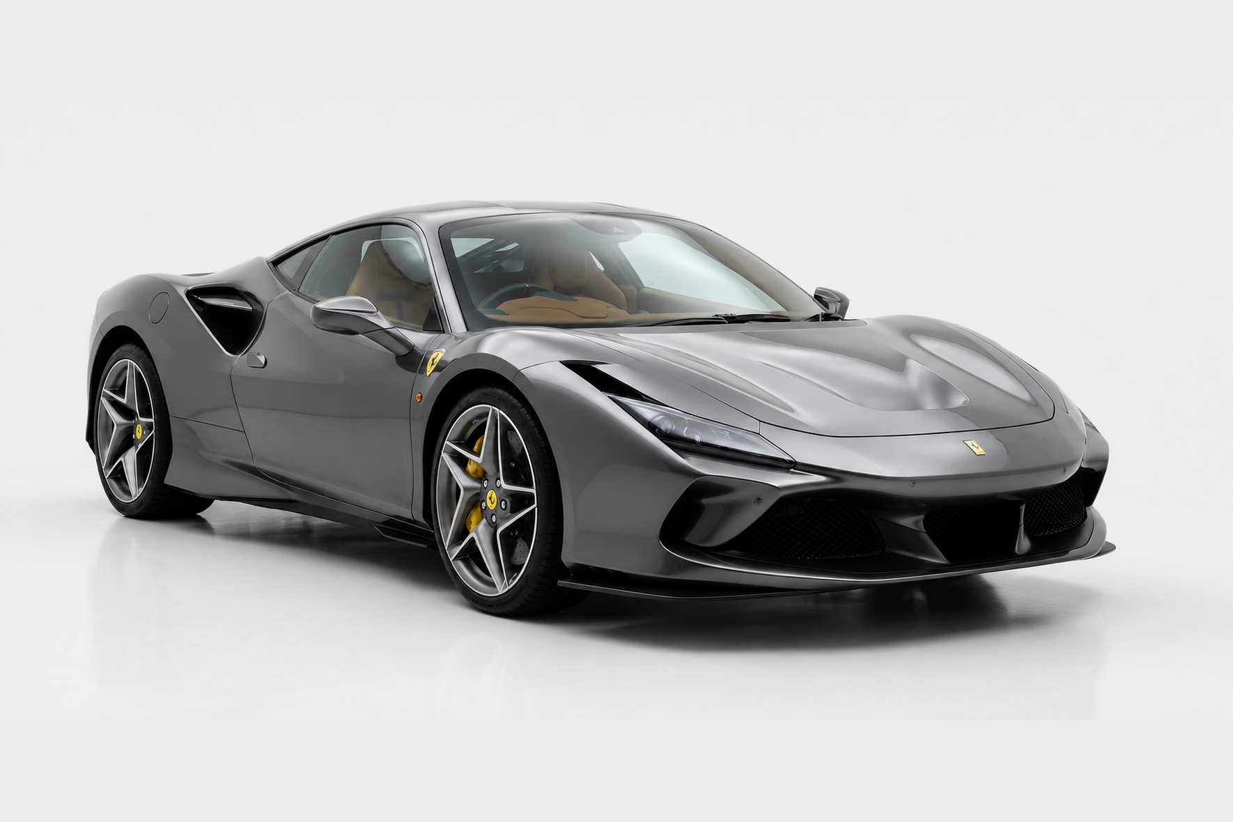 Grigio Silverstone Ferrari F8 Tributo photographed in a studio, front three-quarter view showing the S-Duct front bonnet, black lower splitter, side air intakes, yellow brake calipers and five-spoke diamond-cut alloy wheels.