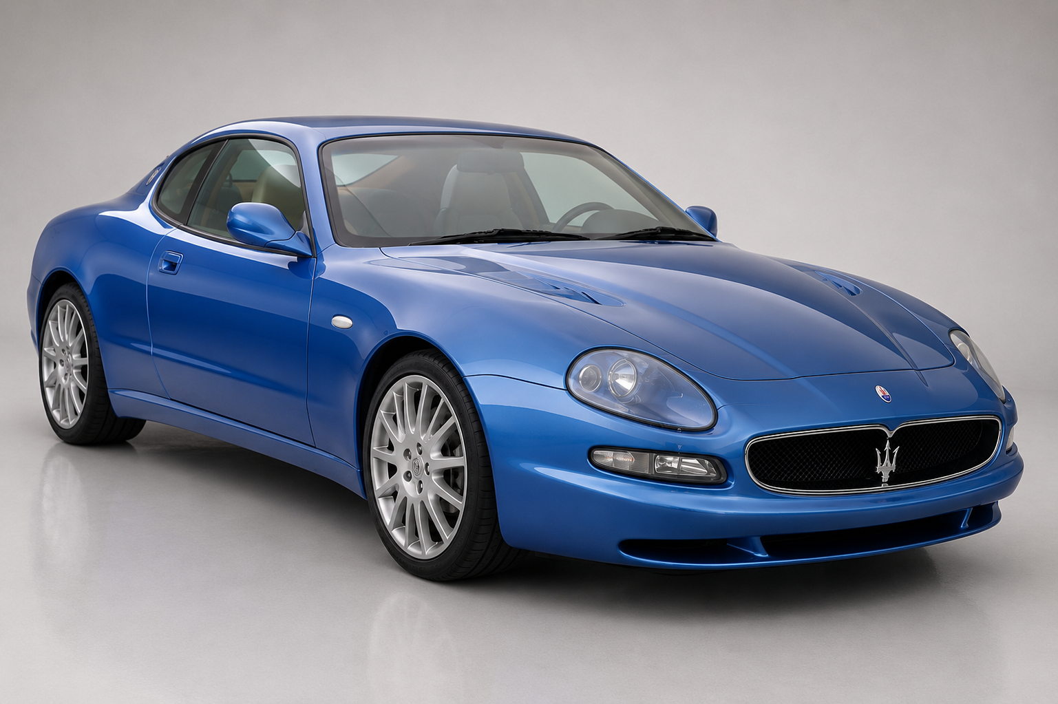 Blue Maserati 3200 GT coupé photographed in a studio, front three-quarter view showing the Giugiaro 2+2 body, oval Trident grille, twin round headlamps under clear covers, side vent and multi-spoke alloy wheels.