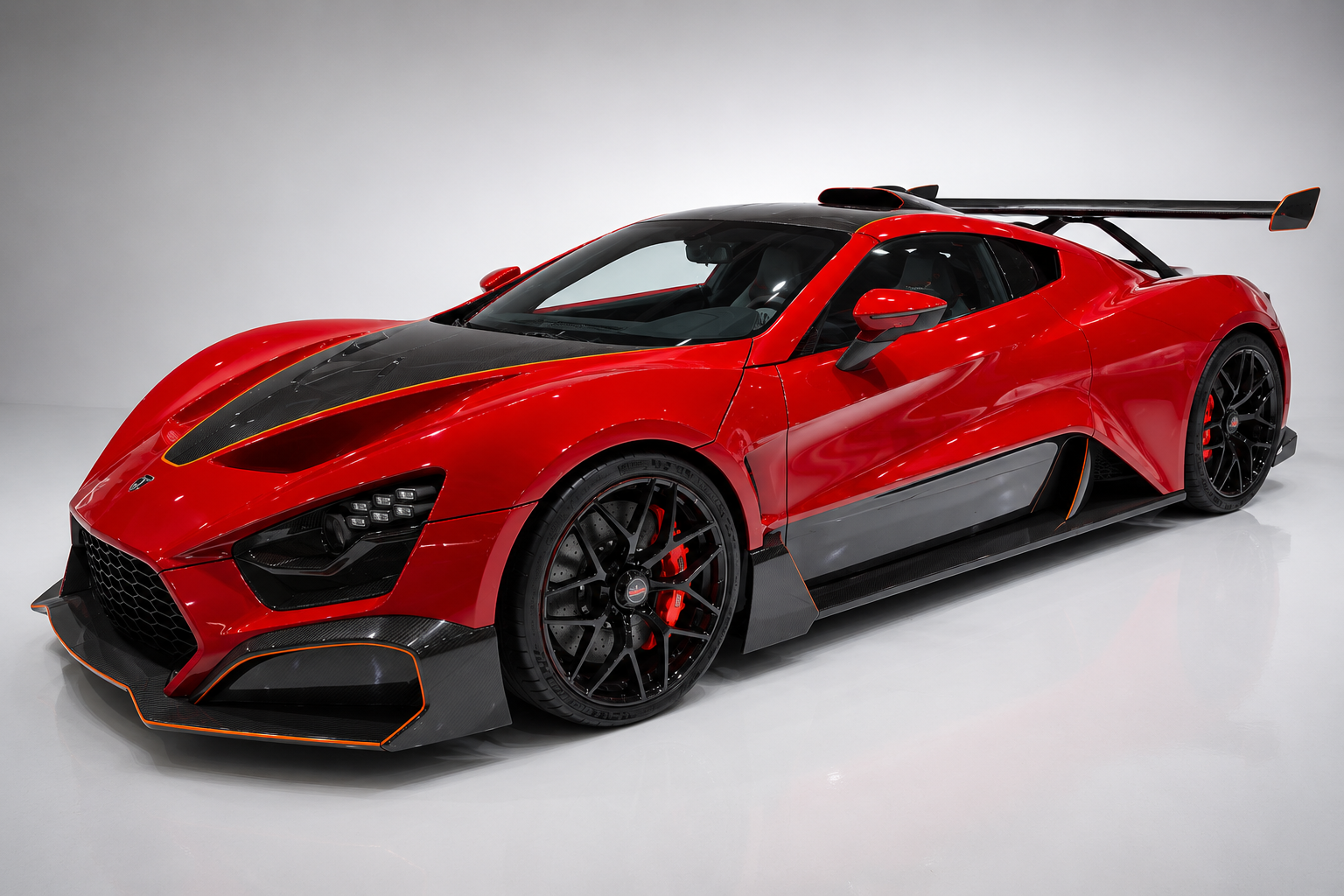 Red Zenvo TSR-S hypercar with exposed carbon-fibre accents, large rear centripetal wing, and black alloy wheels, shown in studio lighting.