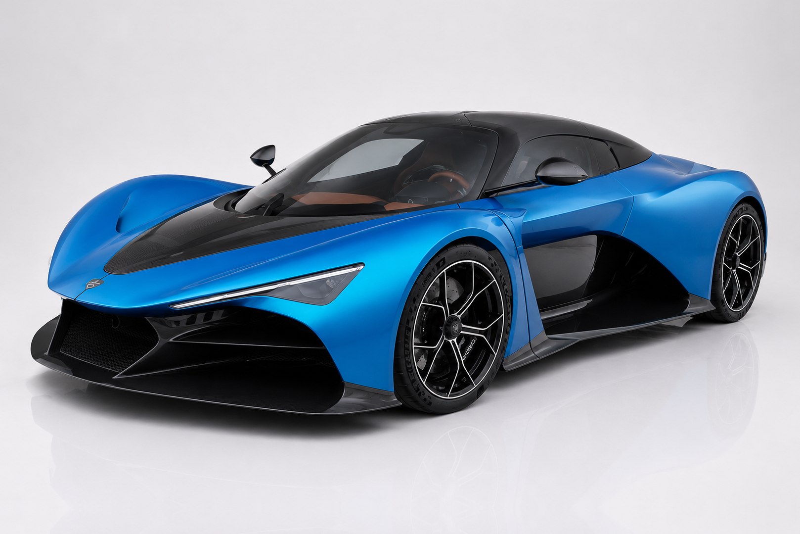 Blue Zenvo Aurora hybrid hypercar in a studio setting, front three-quarter view showing the low mid-engine silhouette, exposed carbon-fibre roof panel and side vents, aggressive front splitter and multi-spoke black alloy wheels.