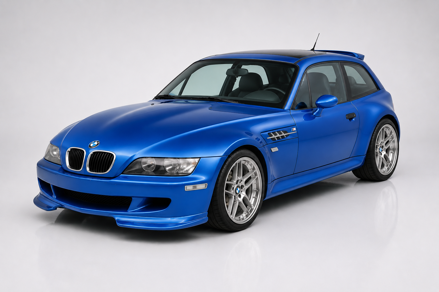 Bright blue BMW Z3 M Coupé, front three-quarter view in a studio, showing the shooting-brake roofline, kidney grille, M gill vents on the front wing, a front splitter and silver double-spoke wheels.