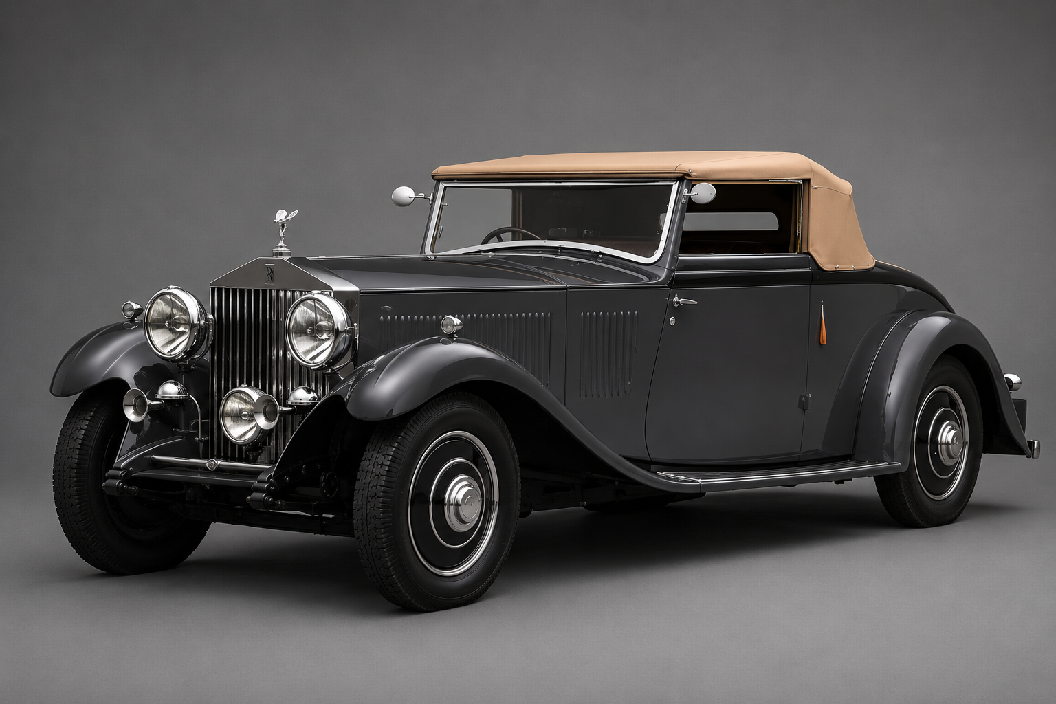 Dark grey pre-war Rolls-Royce Phantom drophead coupe with tan canvas hood raised, front three-quarter studio view on a plain grey backdrop showing the tall chrome radiator, Spirit of Ecstasy mascot, twin chrome headlamps with driving lamp between, side-mounted spare wheel and black wings.