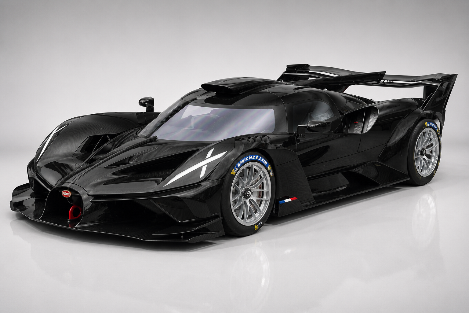 Black Bugatti Bolide track-only hypercar in a studio setting, front three-quarter view showing carbon-fibre bodywork, dramatic X-shaped headlights, massive rear wing, Michelin racing tyres and the low-slung LMP-inspired proportions.