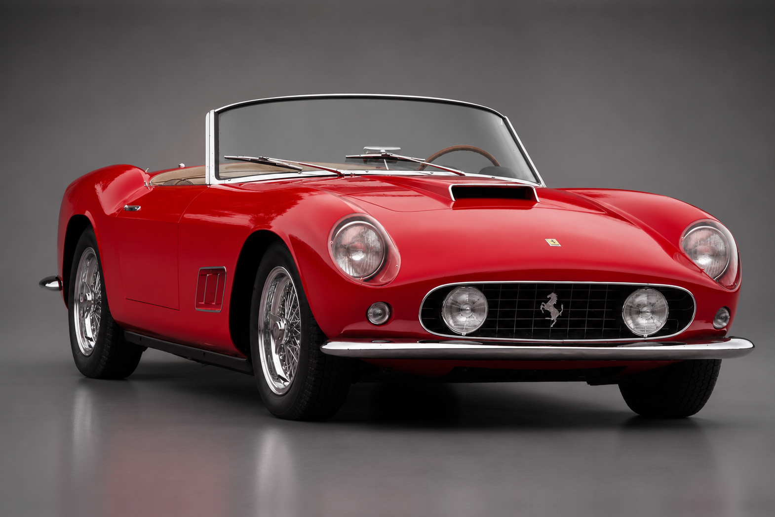 Red Ferrari 250 GT California Spider with tan interior, front three-quarter studio view on a grey backdrop showing the open-headlamp nose, chromed grille with prancing horse badge, wire wheels and full-width windscreen.
