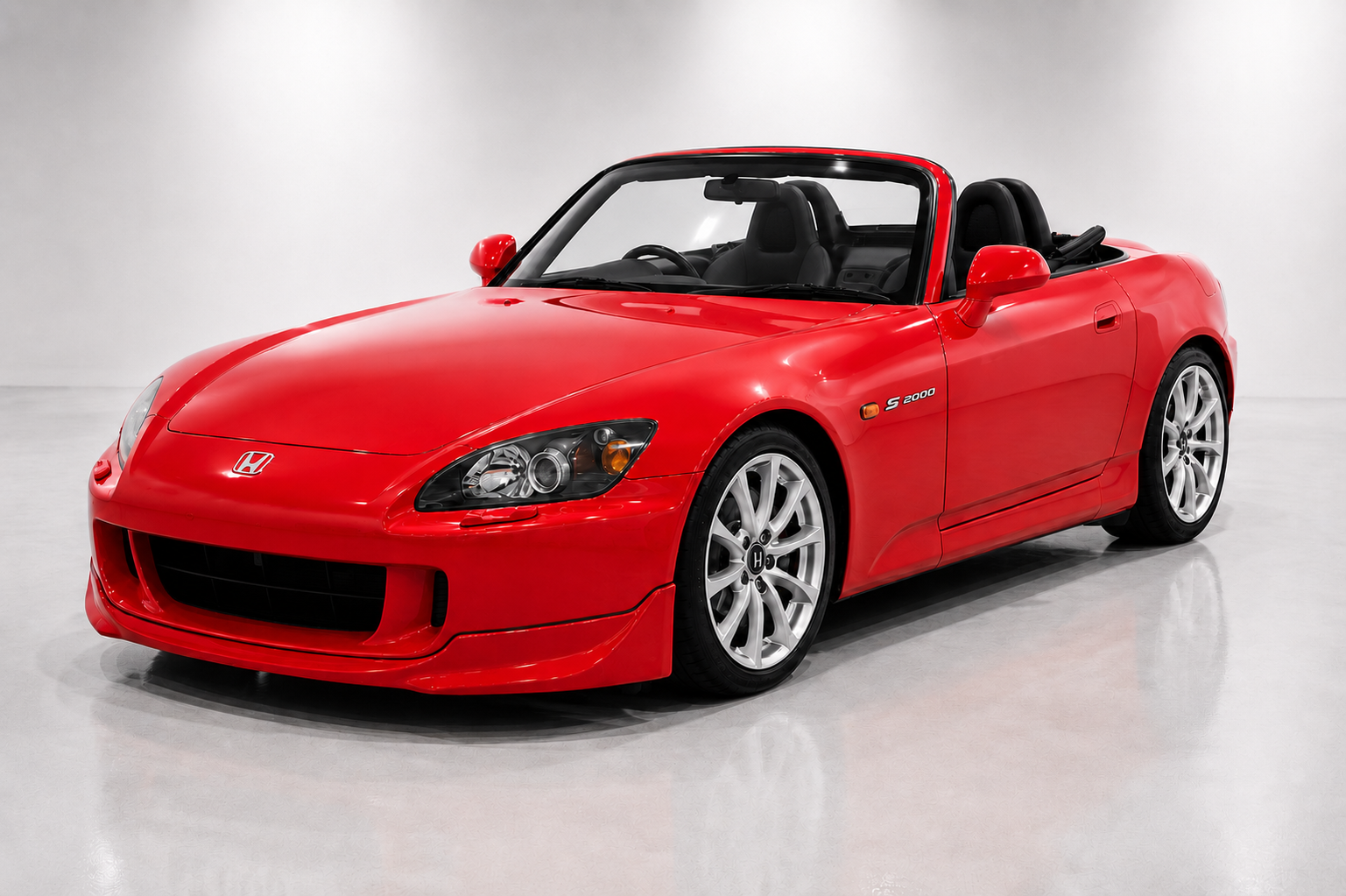 Red Honda S2000 AP2 roadster with the roof down in a studio setting, showing the long nose, compact cabin, five-spoke alloy wheels and S2000 side badge.