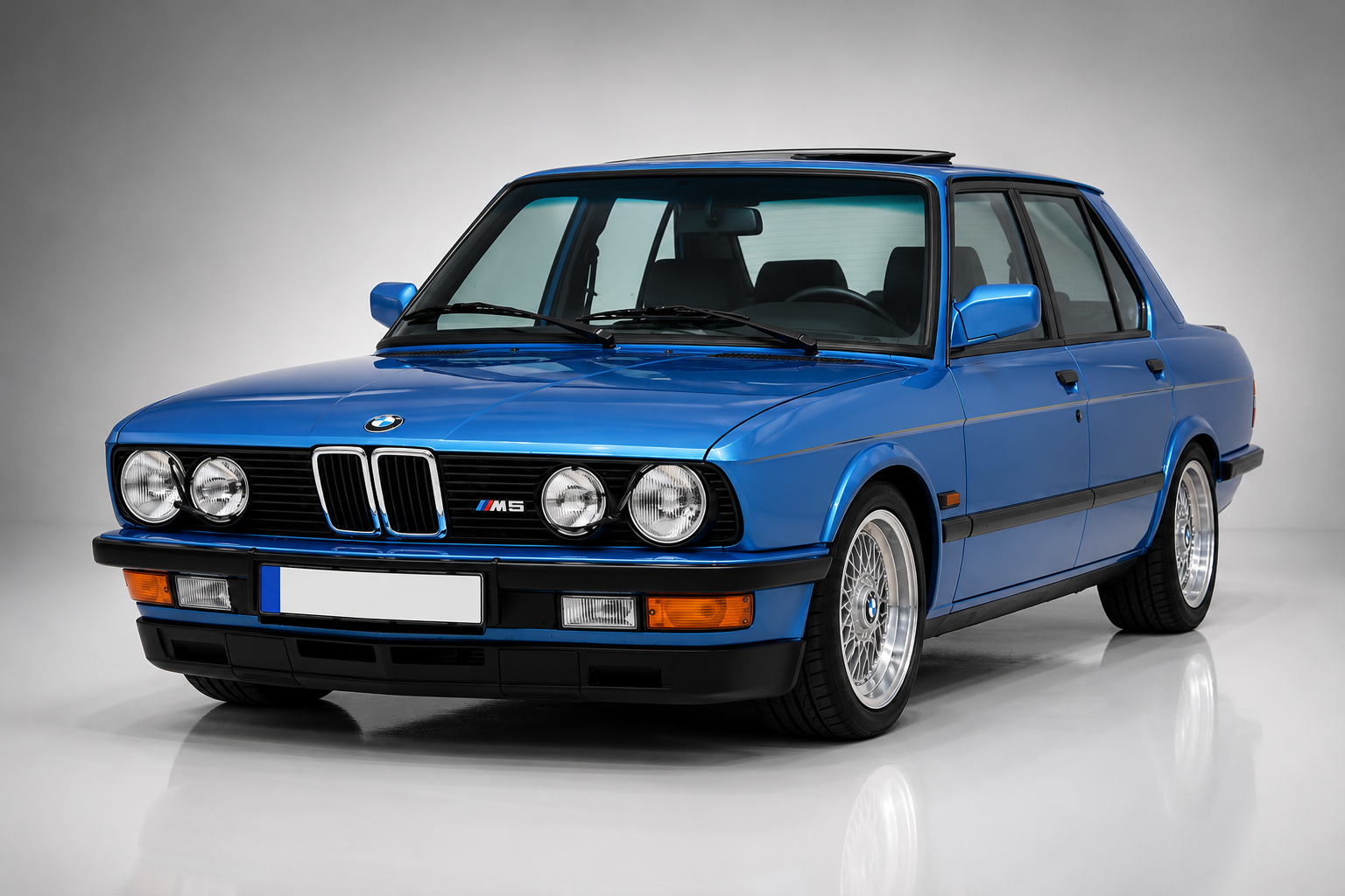 Blue BMW M5 (E28) in a studio setting, front three-quarter view showing the classic four-headlamp face, M5 grille badge, kidney grilles, chrome window trim, alloy wheels and the understated executive-saloon proportions.