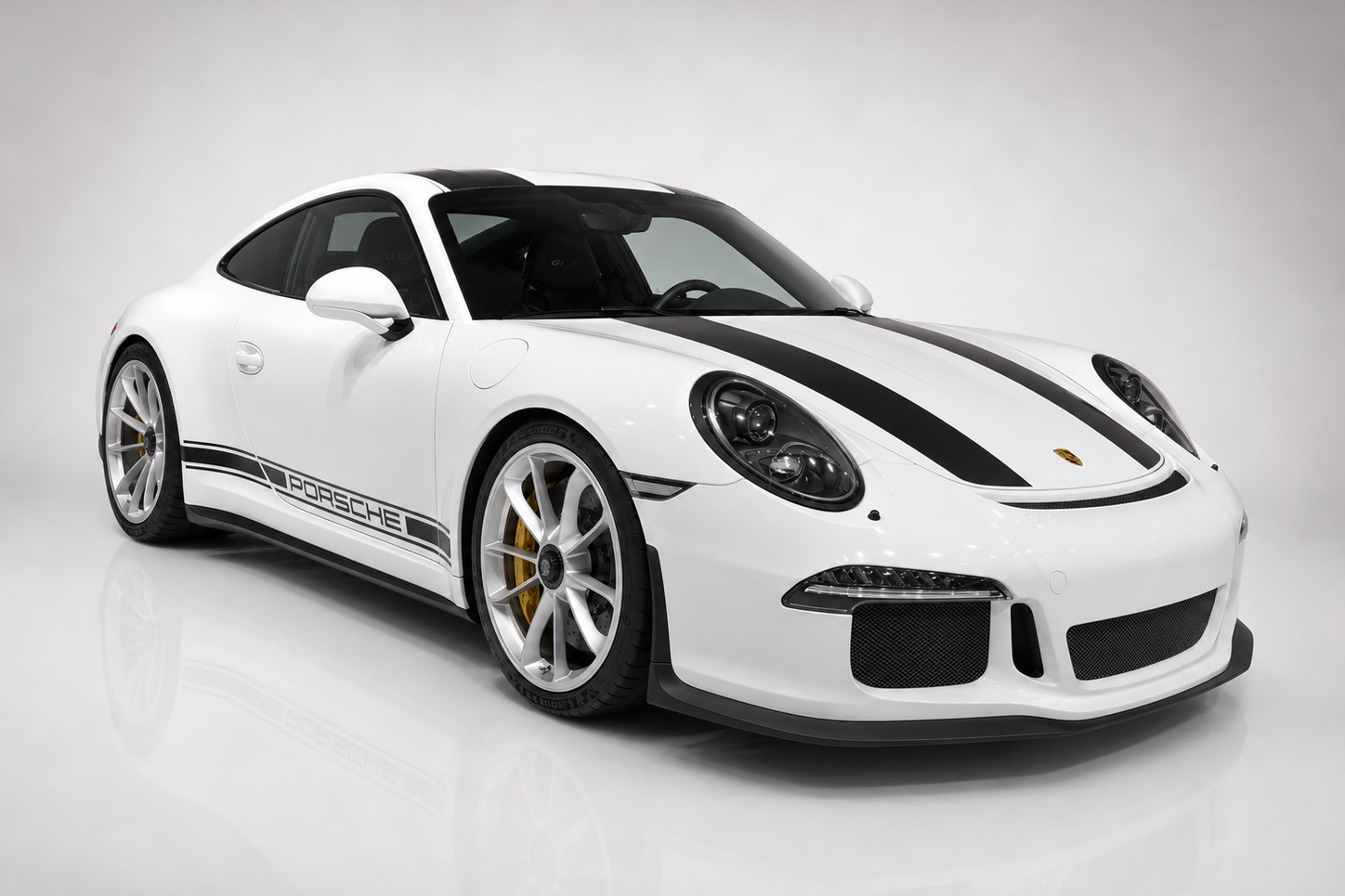 White Porsche 911 R with black centre stripes in a studio, front three-quarter view showing the GT3-based wide body without a rear wing, silver forged wheels and low front splitter.