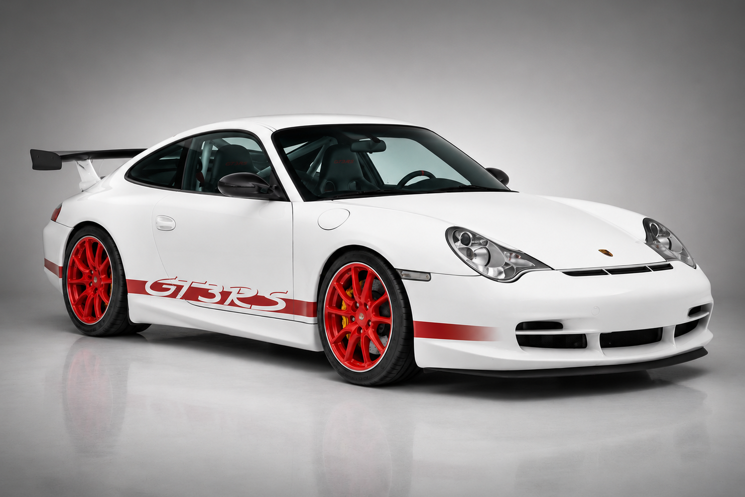 White Porsche 911 GT3 RS (996) in a studio setting, front three-quarter view showing the red side script, red centre-lock-style alloy wheels and fixed carbon rear wing.