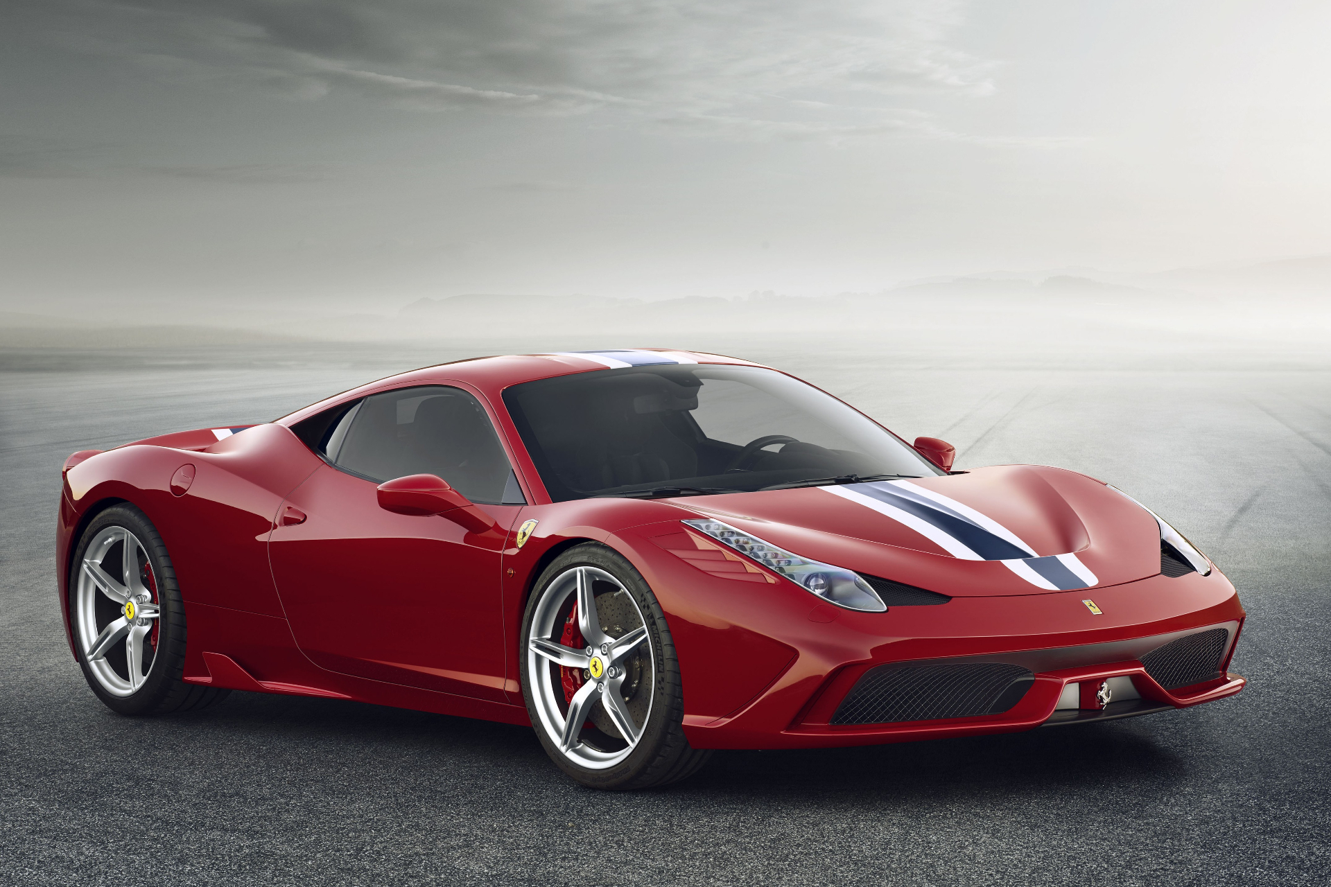 Red Ferrari 458 Speciale with blue and white centre stripes, front three-quarter studio view on tarmac against a misty grey sky, showing the aggressive front splitter, side sill, silver five-spoke alloy wheels and red brake calipers.