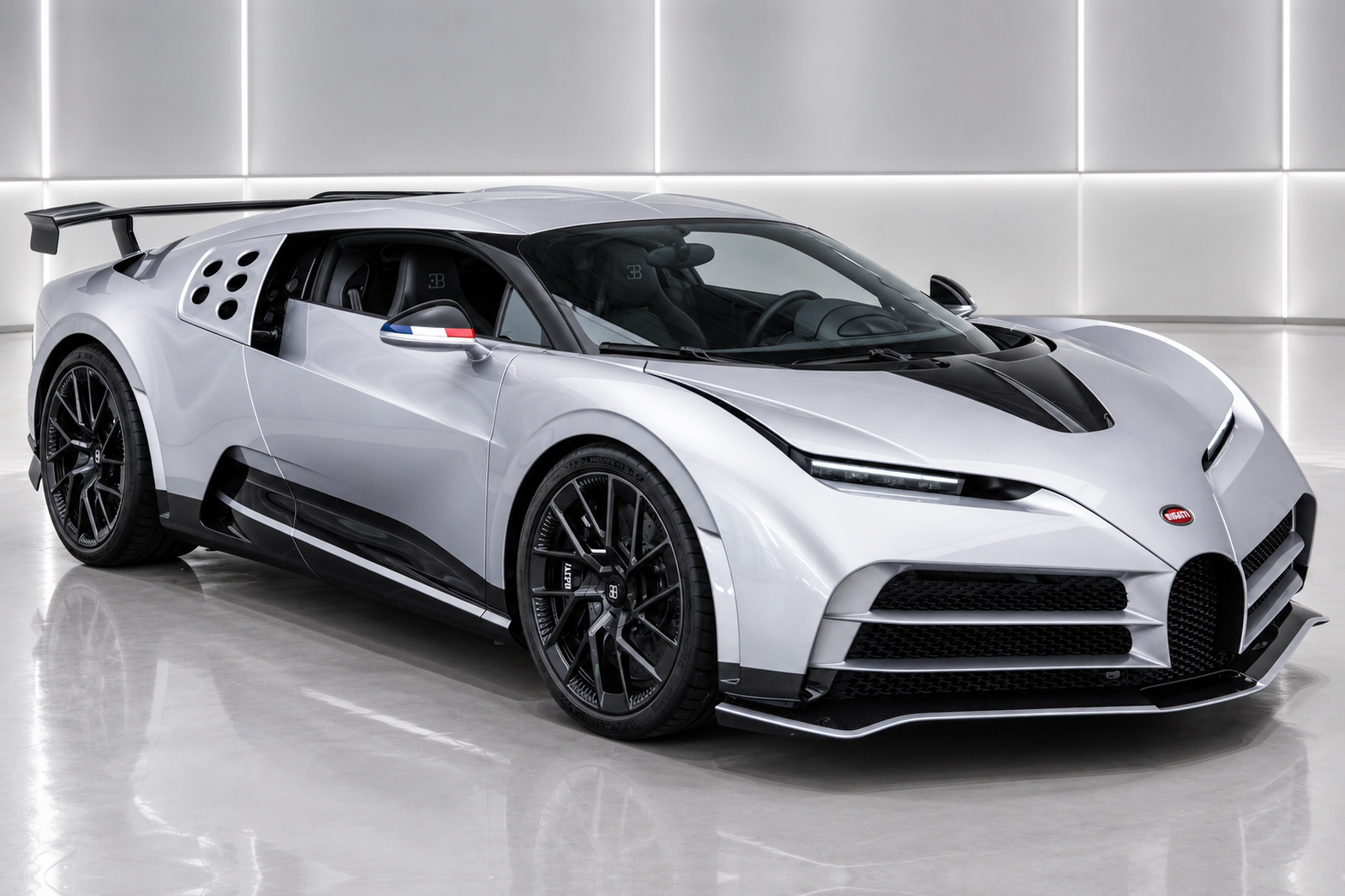 Silver Bugatti Centodieci hypercar in a bright white studio, front three-quarter view showing the EB110-inspired wedge profile, five circular side air intakes, black bonnet stripe, rear wing, French tricolour side-mirror detail and black multi-spoke alloy wheels.