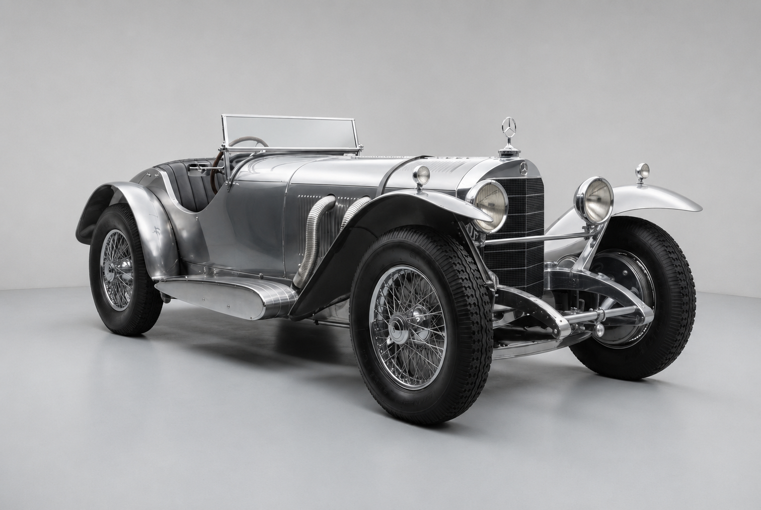 Studio three-quarter front view of a deep-red Mercedes-Benz SSK open two-seater with polished exposed exhaust pipes down the bonnet side, wire wheels, mesh grille and Mercedes-Benz badge, on a plain grey backdrop.