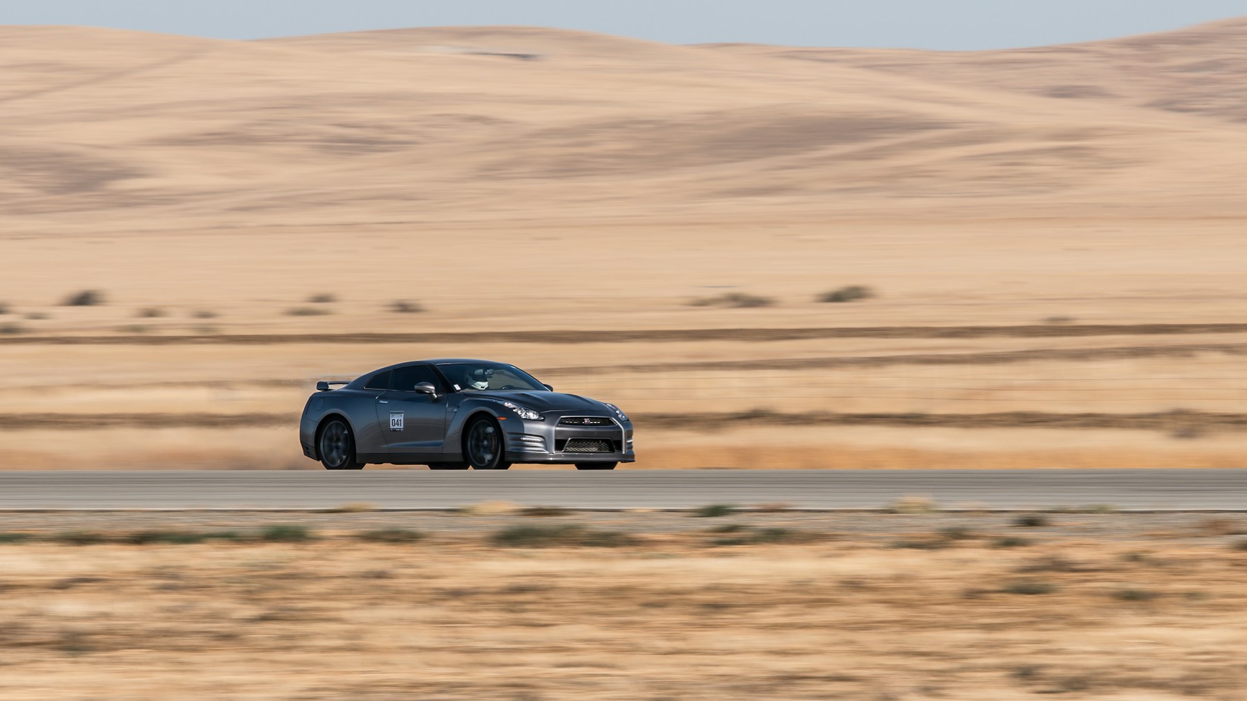 A supercar travelling along an open desert highway in the American Southwest.