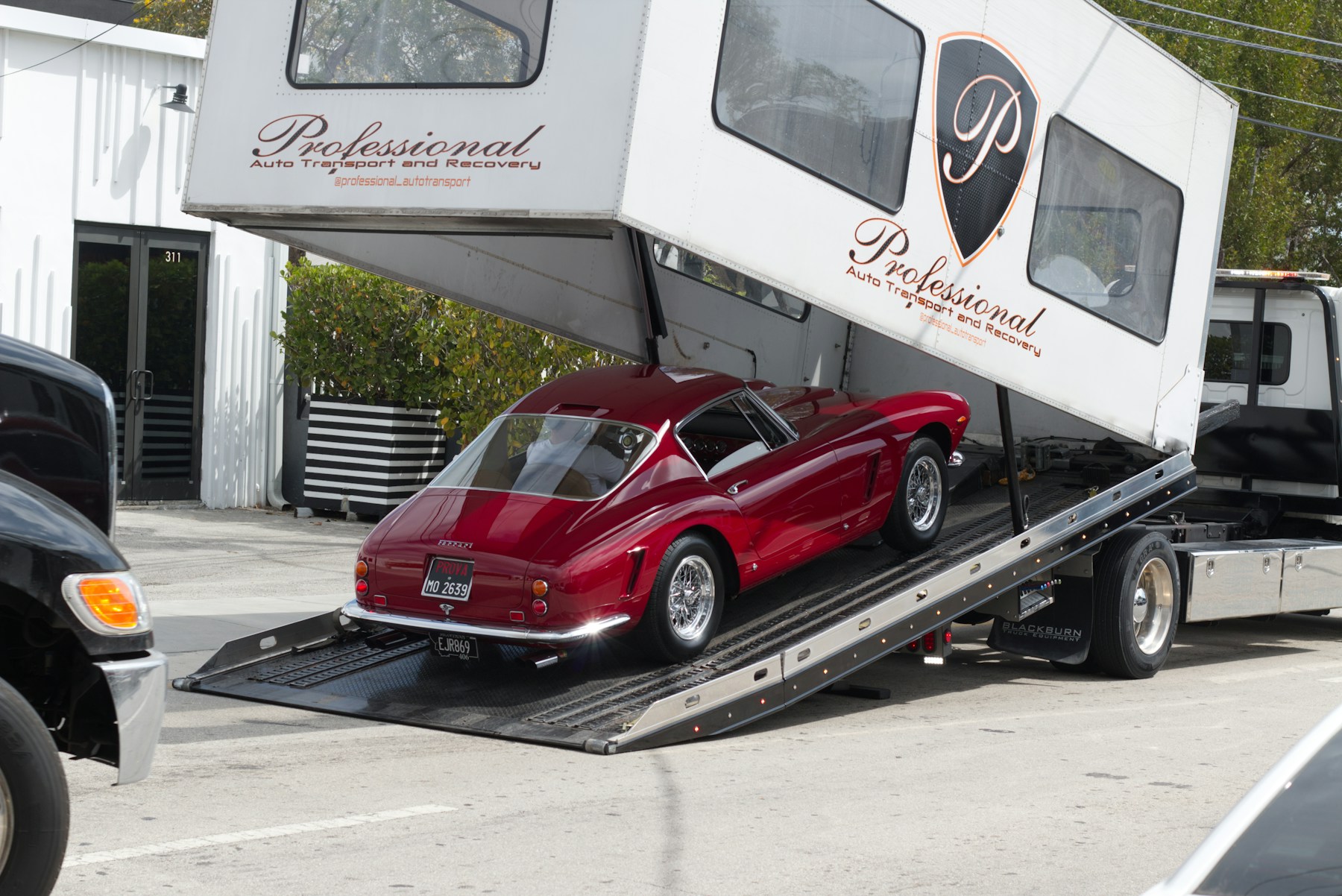 A classic sports car being loaded into an enclosed transport trailer at dusk.